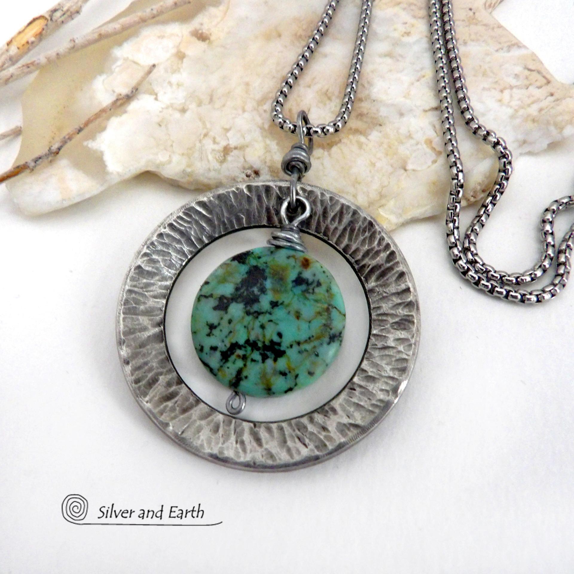 This handcrafted pendant necklace features a natural coin-shaped African turquoise gemstone framed against a hammered and oxidized silver tone pewter circle. It has a modern earthy organic style that coordinates well with all wardrobe types. The design is versatile and can be worn by either a man or woman. It will make a great gift for anyone that loves natural stone jewelry. Handmade in the USA by Silver and Earth Jewelry. 