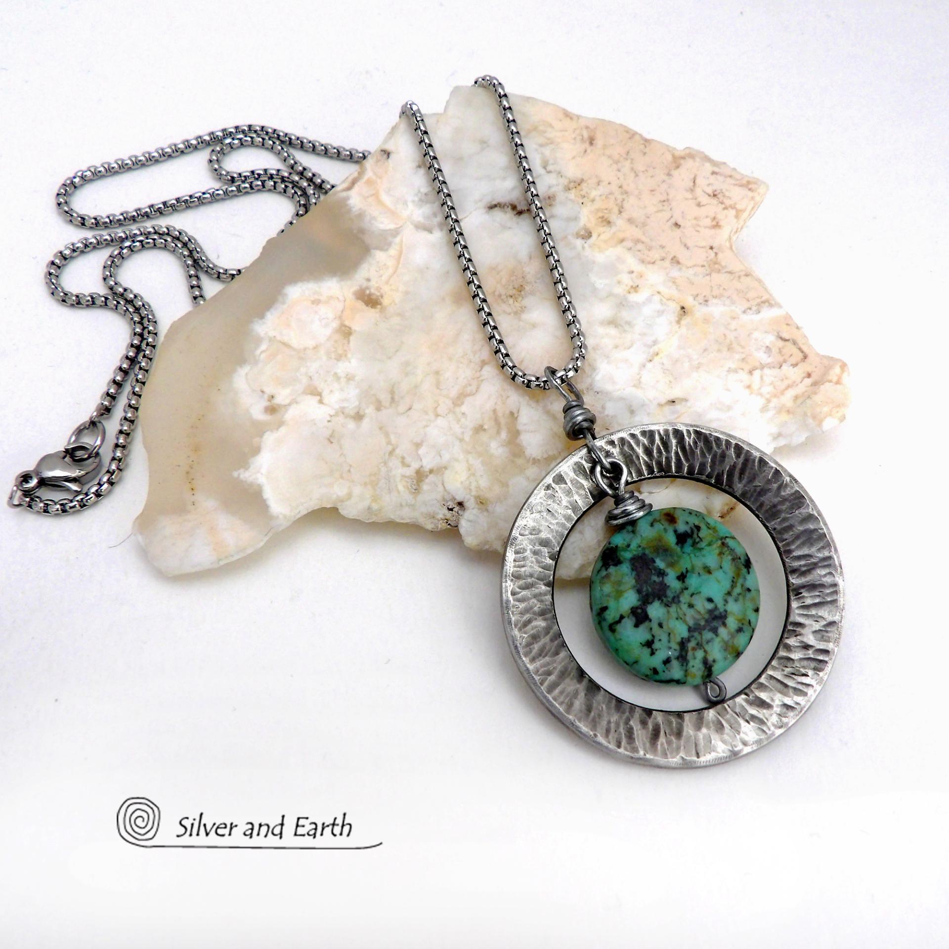 This handcrafted pendant necklace features a natural coin-shaped African turquoise gemstone framed against a hammered and oxidized silver tone pewter circle. It has a modern earthy organic style that coordinates well with all wardrobe types. The design is versatile and can be worn by either a man or woman. It will make a great gift for anyone that loves natural stone jewelry. Handmade in the USA by Silver and Earth Jewelry. 