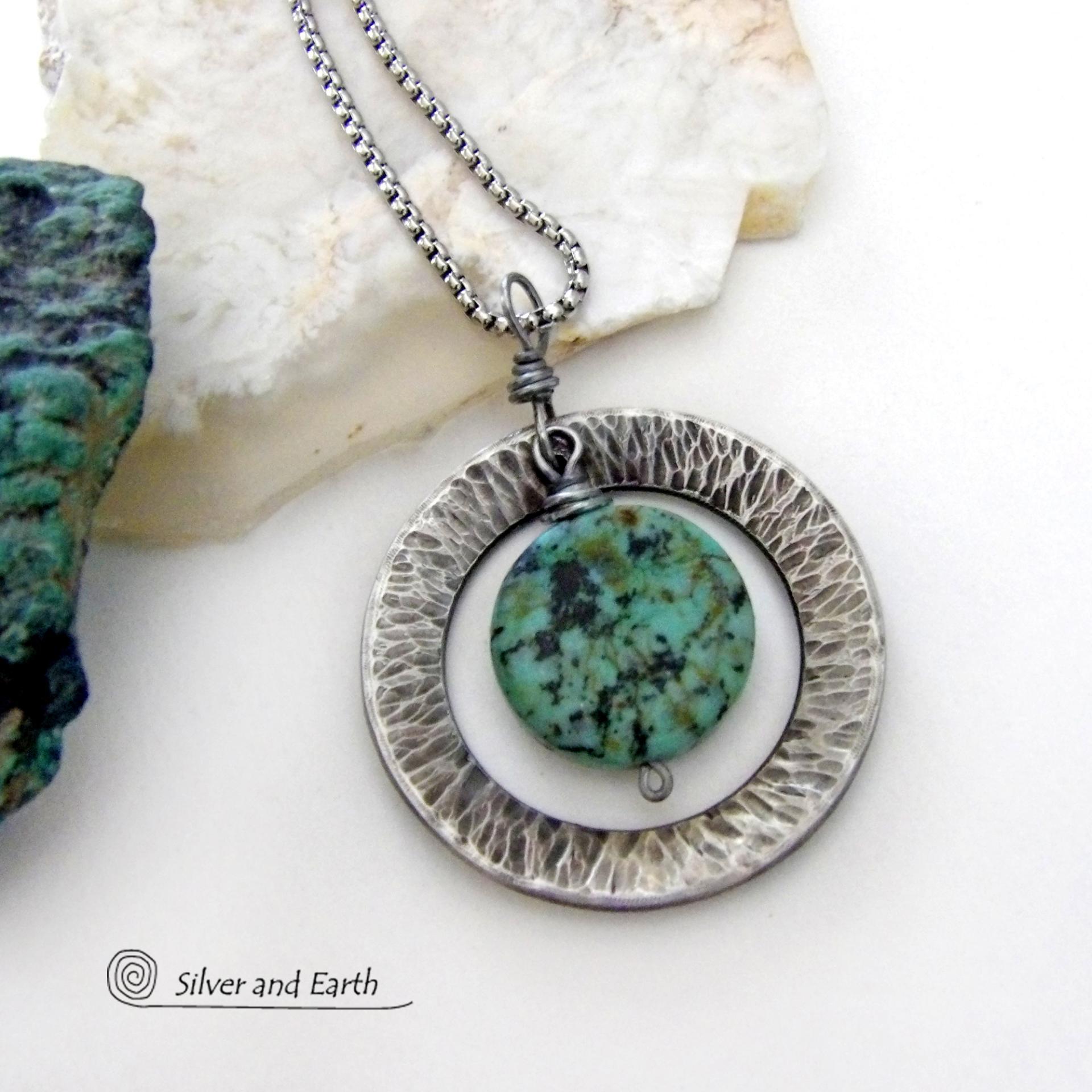 This handcrafted pendant necklace features a natural coin-shaped African turquoise gemstone framed against a hammered and oxidized silver tone pewter circle. It has a modern earthy organic style that coordinates well with all wardrobe types. The design is versatile and can be worn by either a man or woman. It will make a great gift for anyone that loves natural stone jewelry. Handmade in the USA by Silver and Earth Jewelry. 