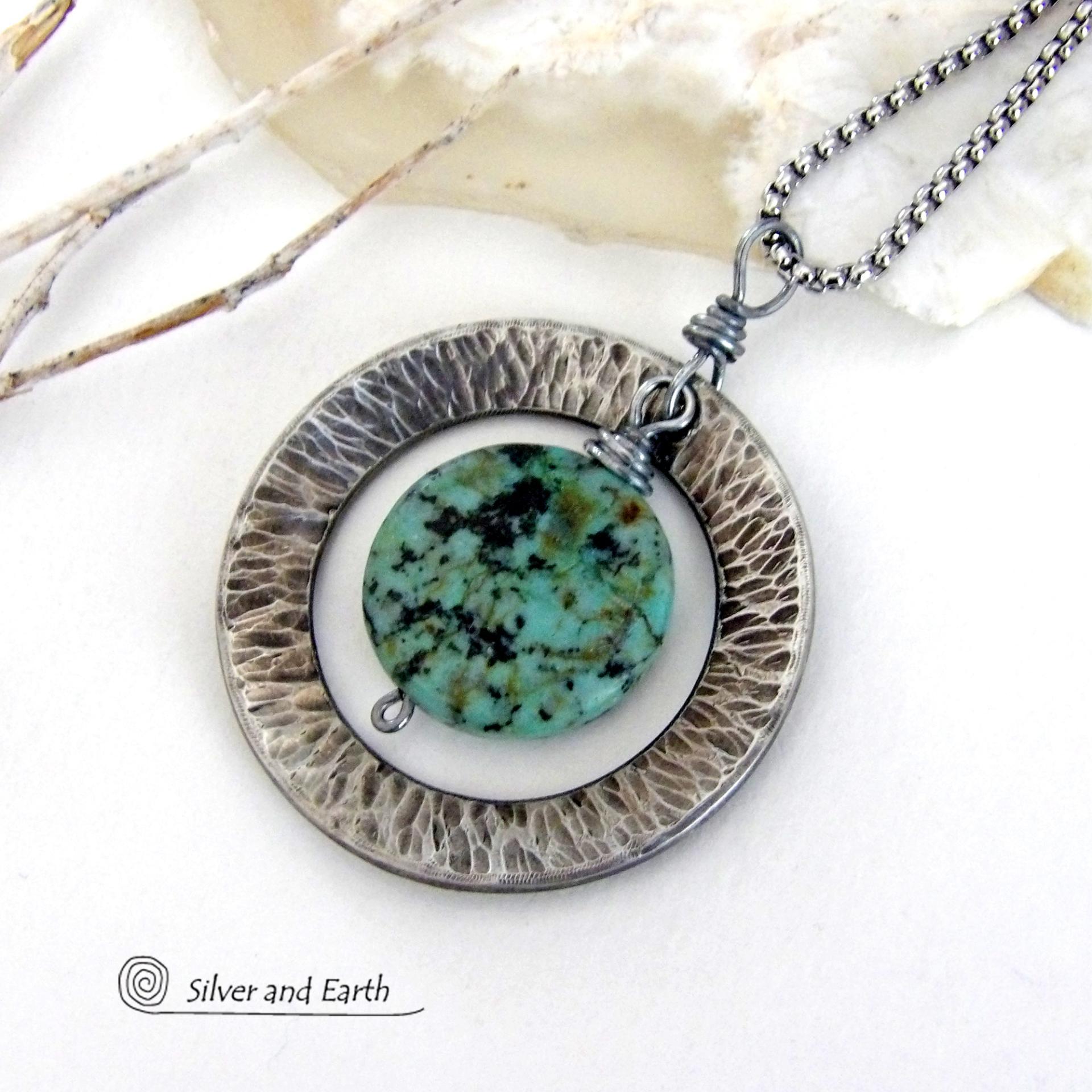 This handcrafted pendant necklace features a natural coin-shaped African turquoise gemstone framed against a hammered and oxidized silver tone pewter circle. It has a modern earthy organic style that coordinates well with all wardrobe types. The design is versatile and can be worn by either a man or woman. It will make a great gift for anyone that loves natural stone jewelry. Handmade in the USA by Silver and Earth Jewelry. 