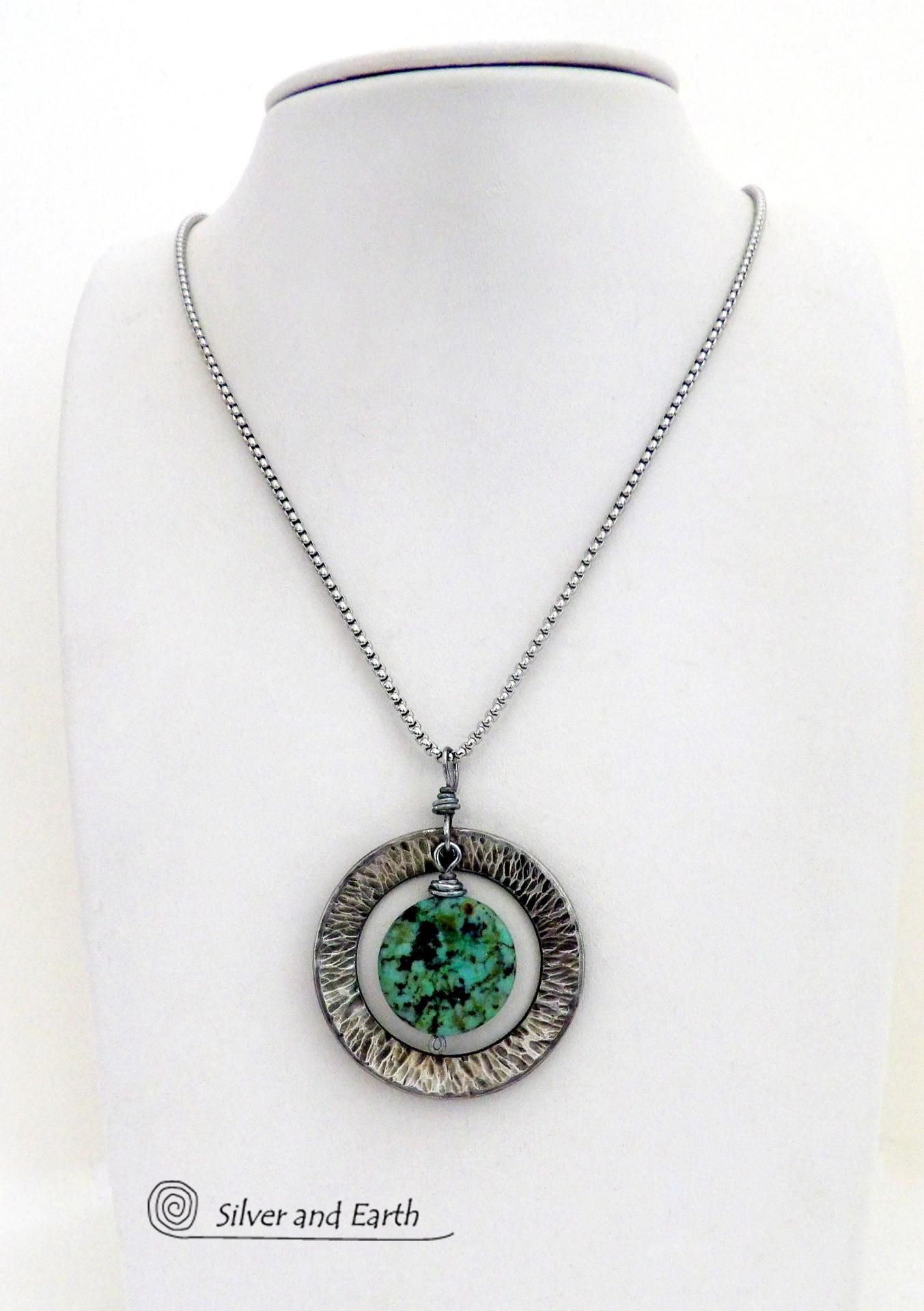 This handcrafted pendant necklace features a natural coin-shaped African turquoise gemstone framed against a hammered and oxidized silver tone pewter circle. It has a modern earthy organic style that coordinates well with all wardrobe types. The design is versatile and can be worn by either a man or woman. It will make a great gift for anyone that loves natural stone jewelry. Handmade in the USA by Silver and Earth Jewelry. 