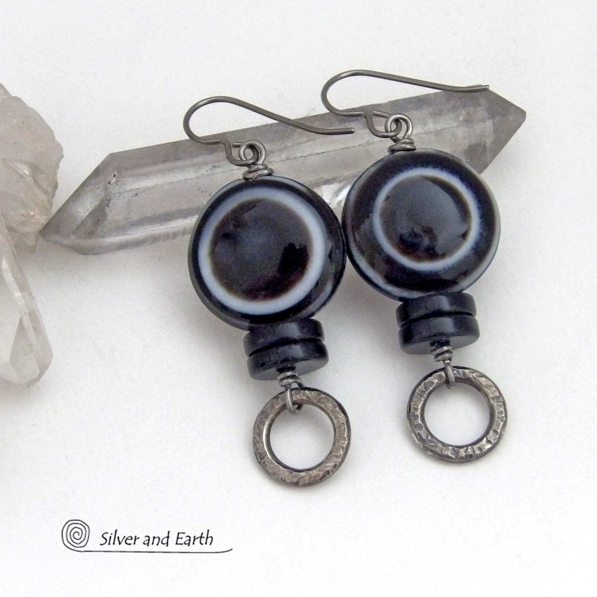 These earrings feature big natural black eye agate stones accented with black onyx and small hammered silver pewter circle dangles. When cut at the right angle, this type of agate reveals a series of concentric rings that resembles the human eye. They have a funky, modern vibe and are unique and fun to wear. They'll make a bold statement and are perfect for women that love to wear unique natural stone jewelry. 