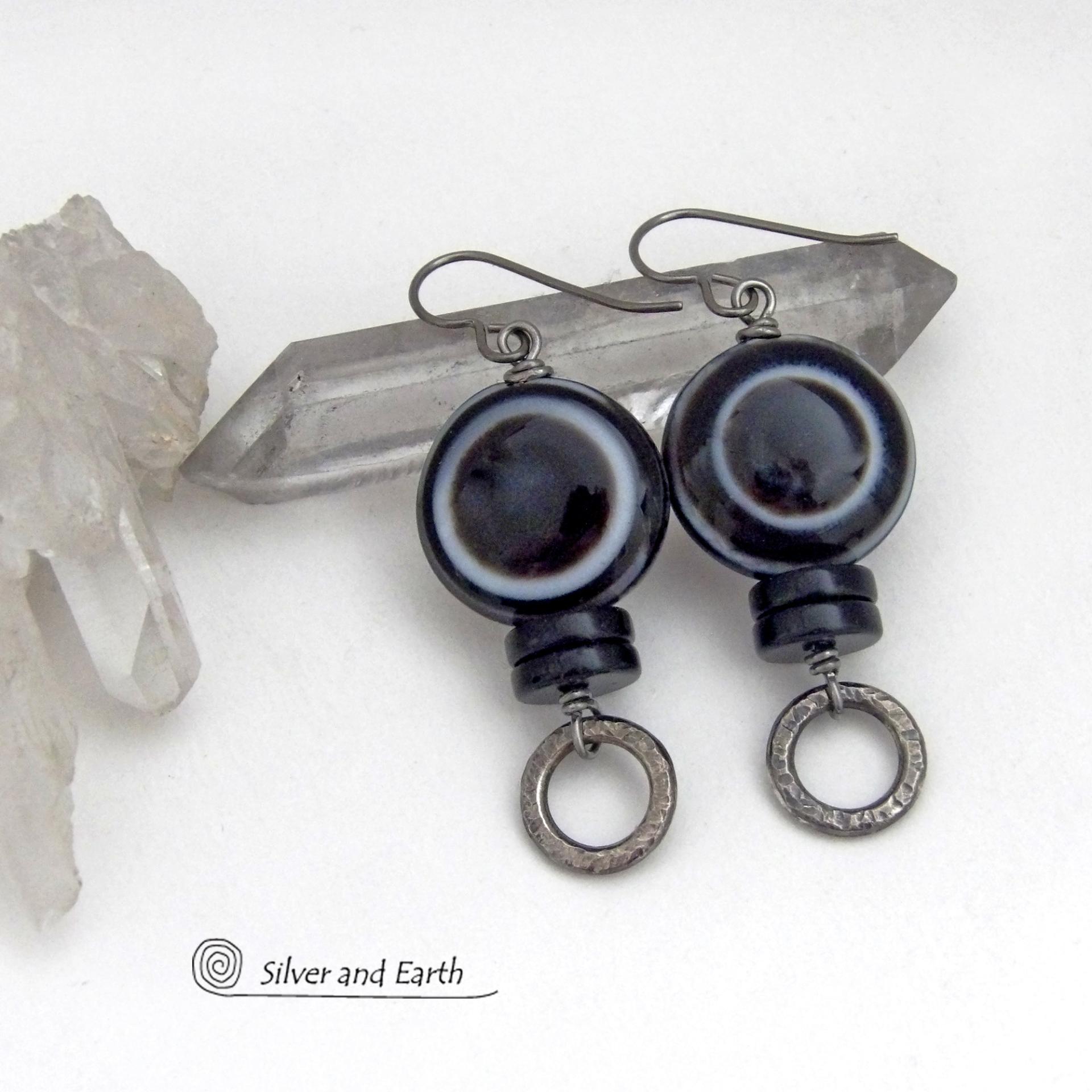 These earrings feature big natural black eye agate stones accented with black onyx and small hammered silver pewter circle dangles. When cut at the right angle, this type of agate reveals a series of concentric rings that resembles the human eye. They have a funky, modern vibe and are unique and fun to wear. They'll make a bold statement and are perfect for women that love to wear unique natural stone jewelry. 
