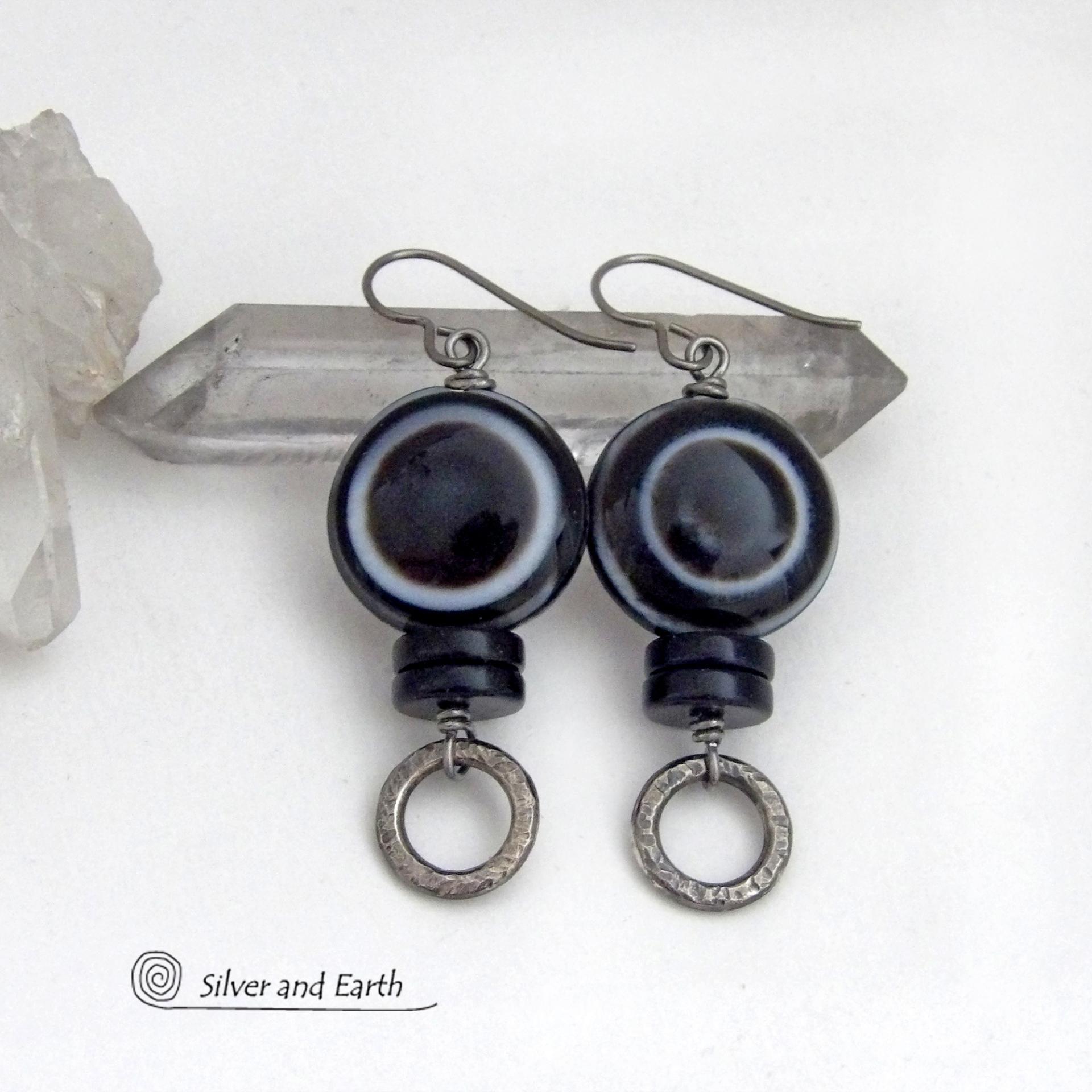 These earrings feature big natural black eye agate stones accented with black onyx and small hammered silver pewter circle dangles. When cut at the right angle, this type of agate reveals a series of concentric rings that resembles the human eye. They have a funky, modern vibe and are unique and fun to wear. They'll make a bold statement and are perfect for women that love to wear unique natural stone jewelry. 