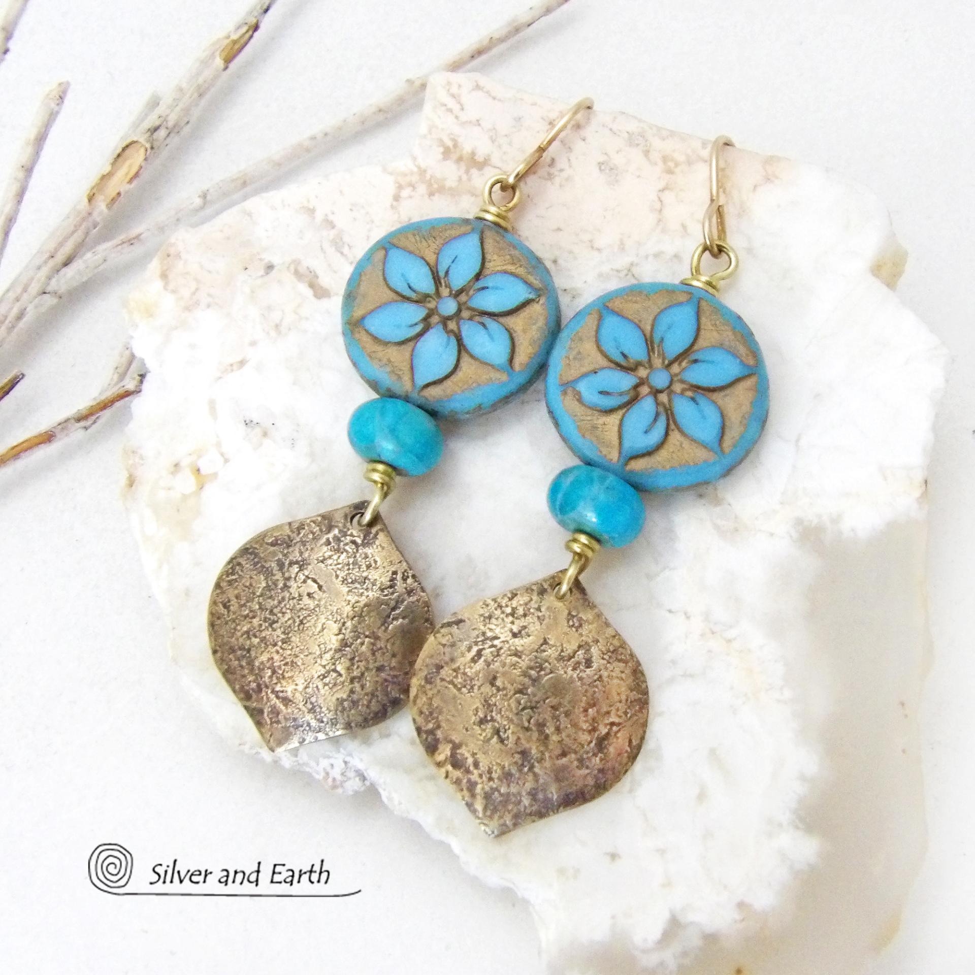 These handcrafted earrings feature gold brass dangles with a lightly hammered raw silk texture accented with glass flower beads and turquoise stone beads. The flower beads are a pretty shade of blue with golden highlights. They have an intricate carved and raised pattern on both sides of the beads. These earrings have a modern elegant, earthy chic style and will make a great gift for anyone that loves flowers and nature. They'll make a great addition to your spring / summer wardrobe - or any time of year.