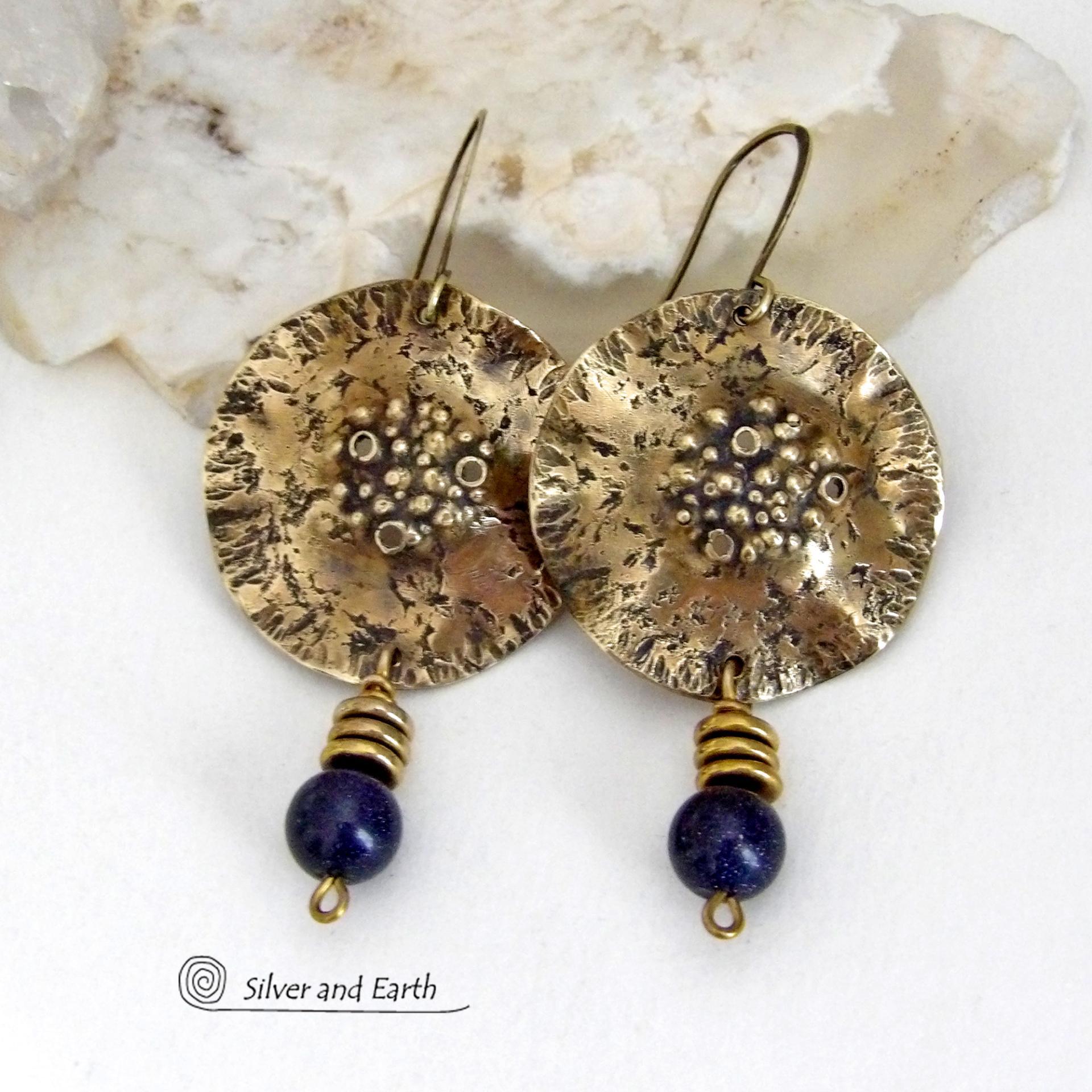These handcrafted gold brass earrings have a rustic, hammered texture and are accented with dangling dark blue goldstones and small brass beads. They have a modern chic style with an earthy, organic vibe. Goldstone is a man-made stone of quartz sand glass infused with copper particles which creates the subtle sparkle effects. It was invented in Venice, Italy in the seventeenth century. These earrings are perfect for women that love unique, bold one-of-a-kind artisan handmade jewelry. 