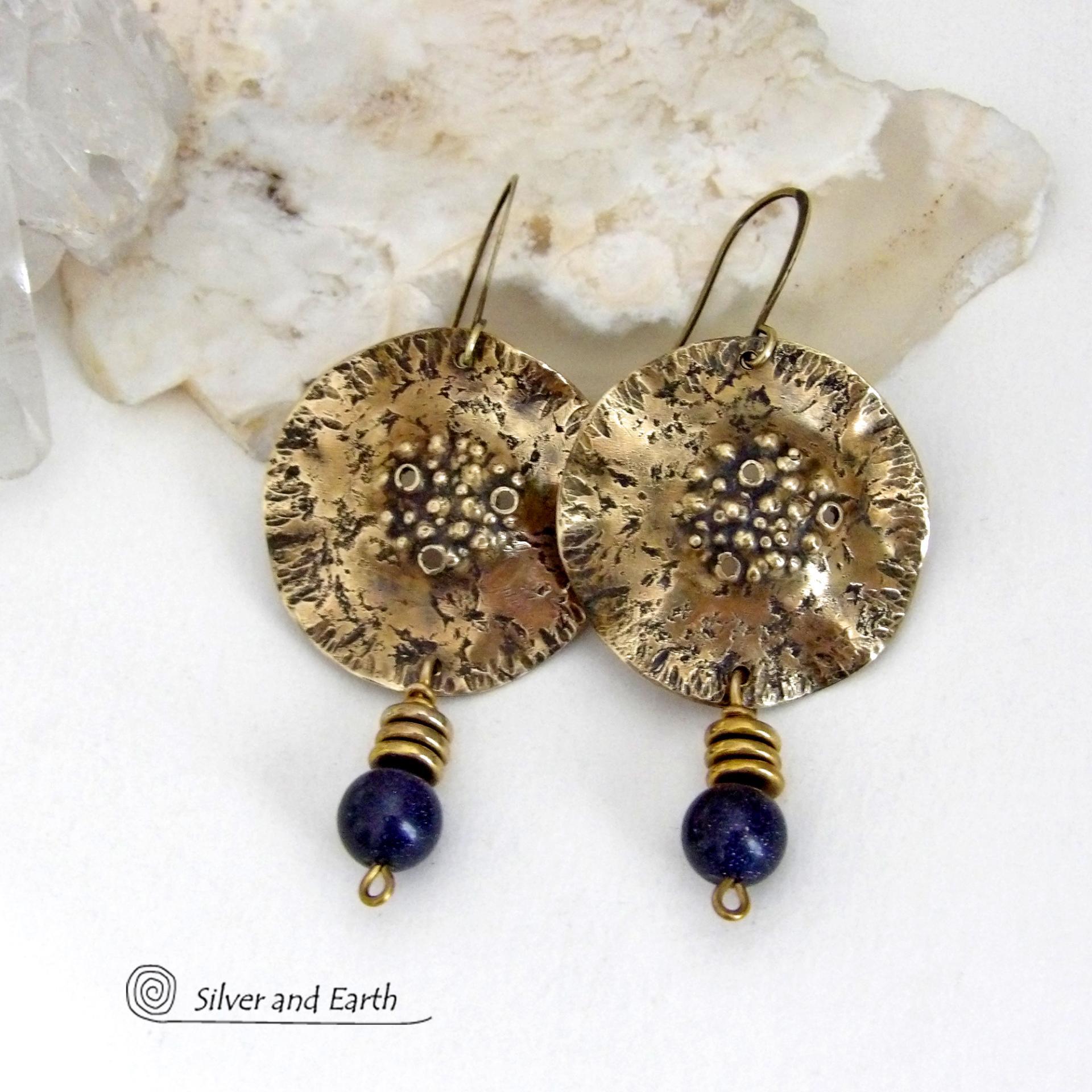 These handcrafted gold brass earrings have a rustic, hammered texture and are accented with dangling blue goldstones and small brass beads. They have a modern chic style with an earthy, organic vibe. Goldstone is a man-made stone of quartz sand glass infused with copper particles which creates the subtle sparkle effects. It was invented in Venice, Italy in the seventeenth century. Handmade in the USA by Silver and Earth Jewelry. 