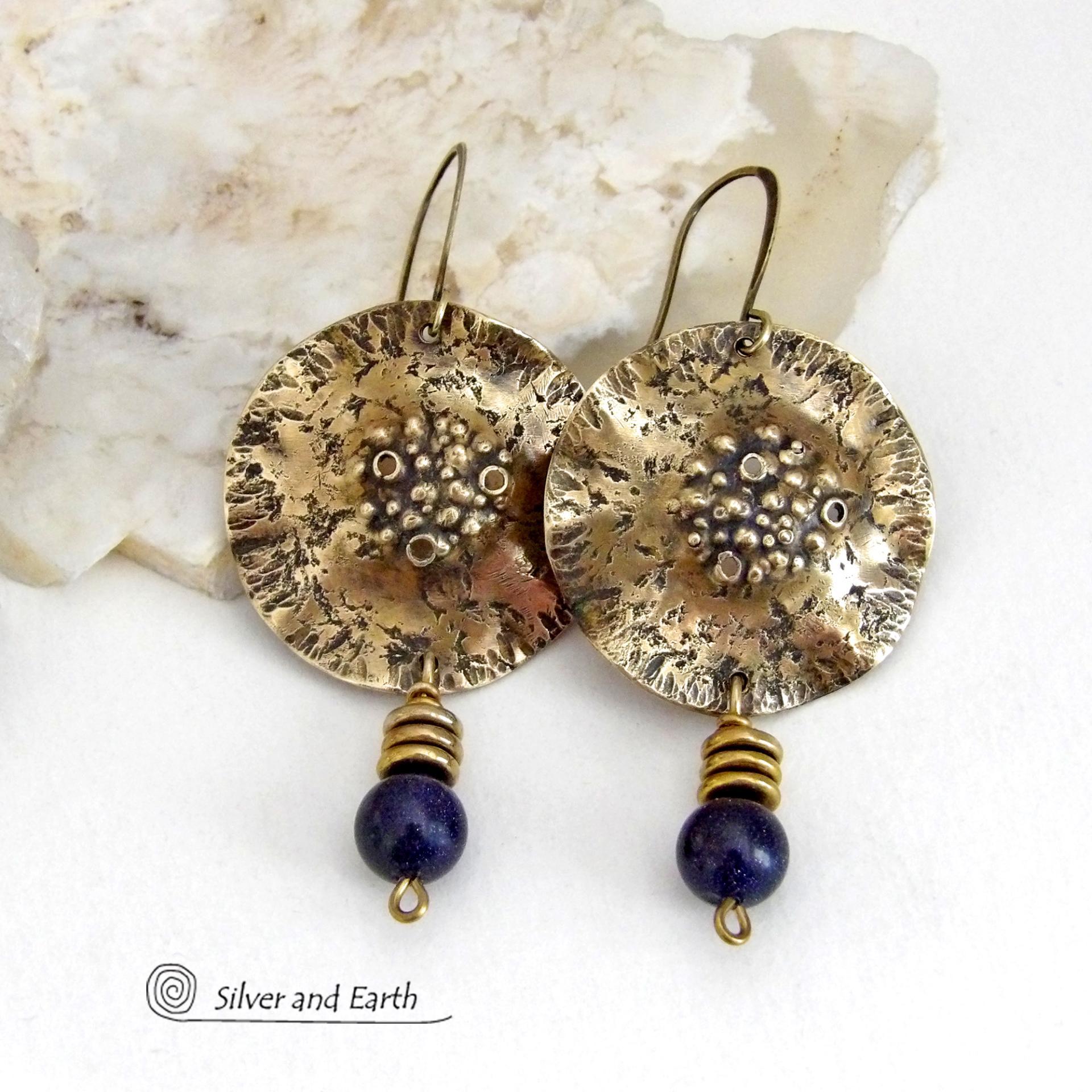 These handcrafted gold brass earrings have a rustic, hammered texture and are accented with dangling blue goldstones and small brass beads. They have a modern chic style with an earthy, organic vibe. Goldstone is a man-made stone of quartz sand glass infused with copper particles which creates the subtle sparkle effects. It was invented in Venice, Italy in the seventeenth century. Handmade in the USA by Silver and Earth Jewelry. 