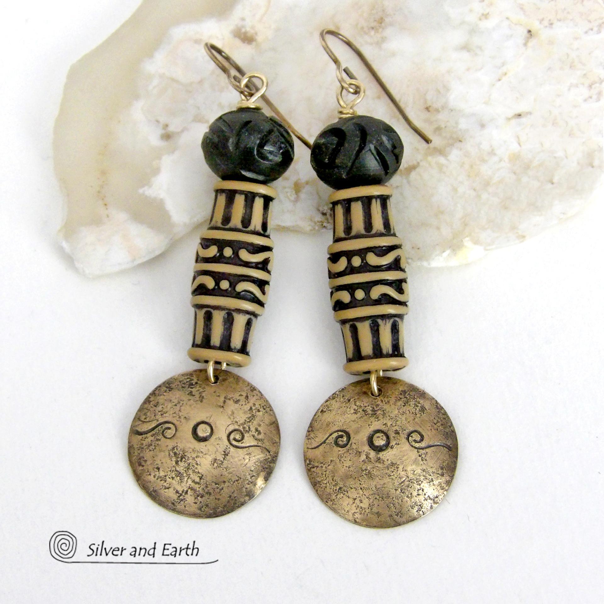 Bold and unique, these handcrafted earrings have an ethnic African tribal vibe. They feature gold brass dangles with a hand stamped and lightly hammered background texture accented with African beads with an intricately carved brownish-black and tan pattern topped off with black African carved bone beads. Unique and fun to wear - they'll make a bold, striking statement. Perfect for women that love to wear one-of-a-kind artisan handcrafted jewelry. Handmade in the USA by Silver and Earth Jewelry.