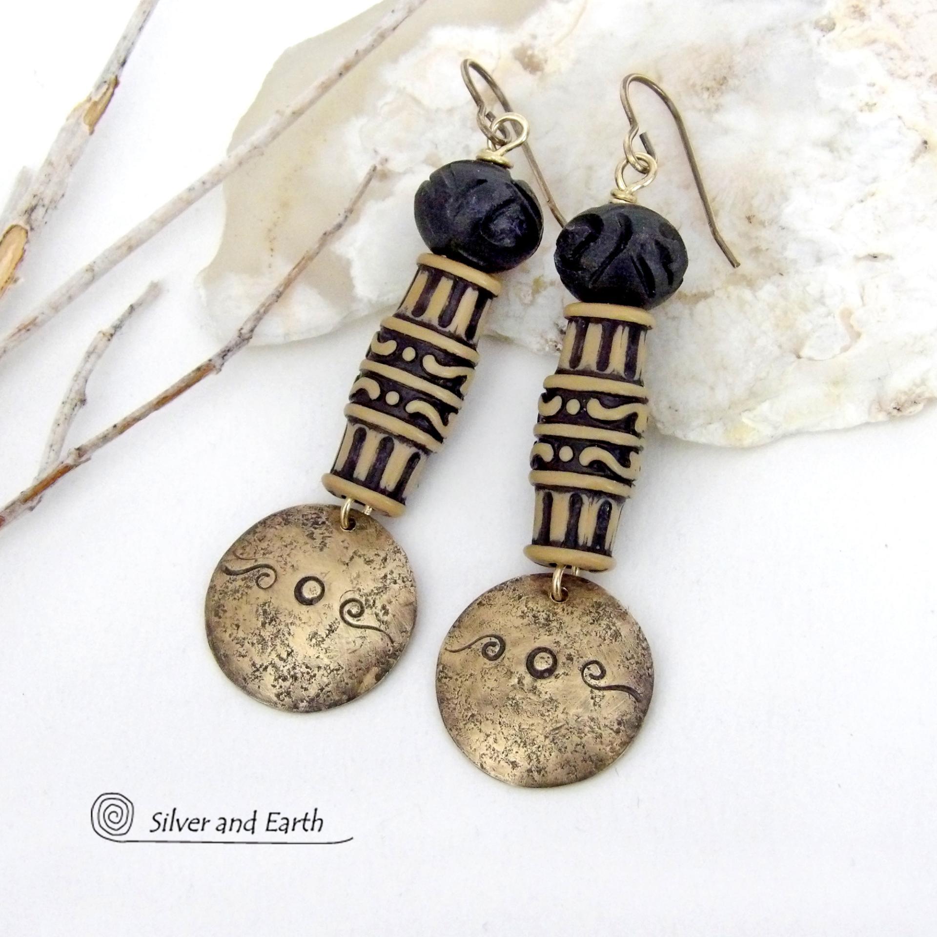 Bold and unique, these handcrafted earrings have an ethnic African tribal vibe. They feature gold brass dangles with a hand stamped and lightly hammered background texture accented with African beads with an intricately carved brownish-black and tan pattern topped off with black African carved bone beads. Unique and fun to wear - they'll make a bold, striking statement. Perfect for women that love to wear one-of-a-kind artisan handcrafted jewelry. Handmade in the USA by Silver and Earth Jewelry.