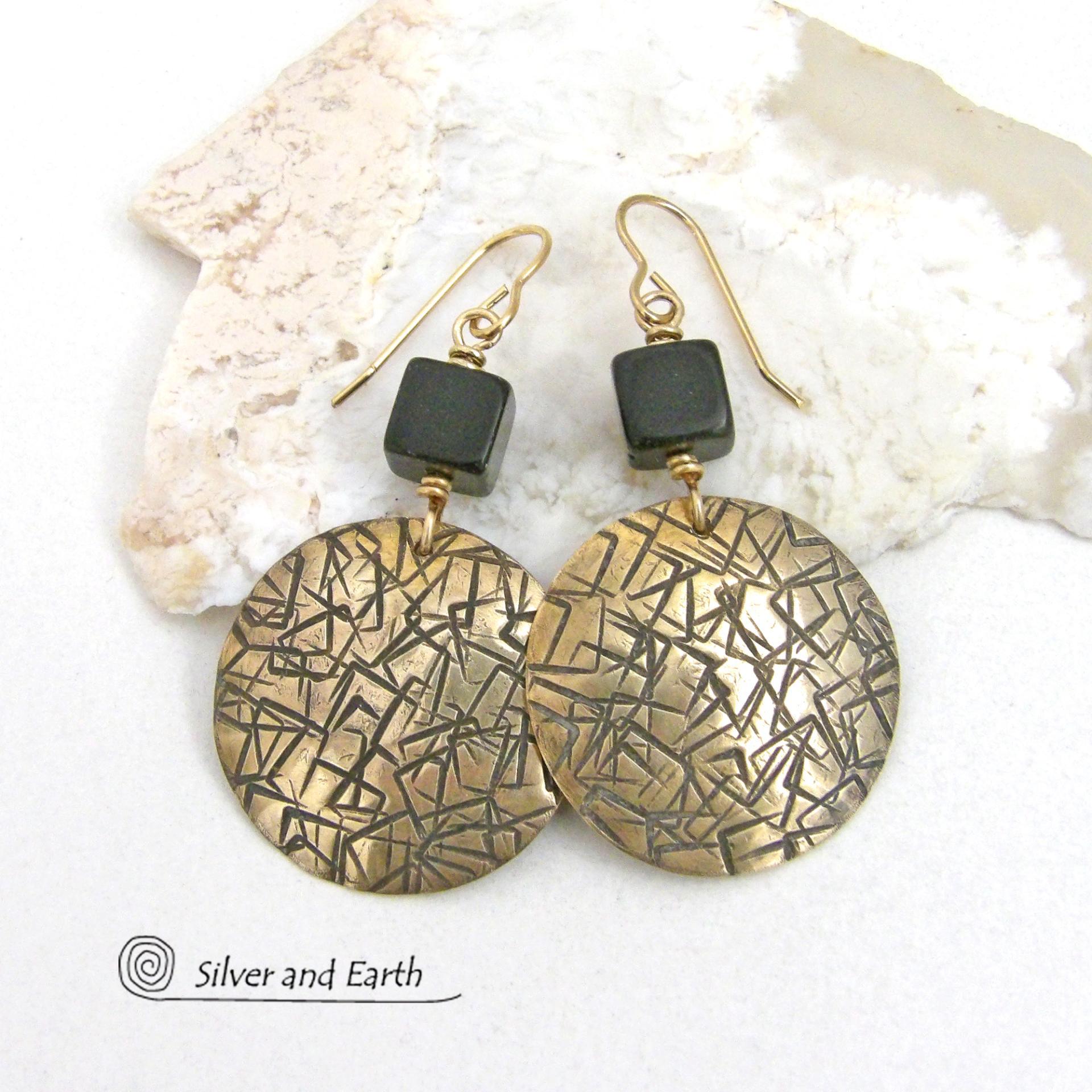 Artisan handcrafted round gold brass earrings with a hand-stamped abstract texture accented with cube-shaped matte black jasper stones on top. They have a modern contemporary vibe that coordinates beautifully with all wardrobe styles.