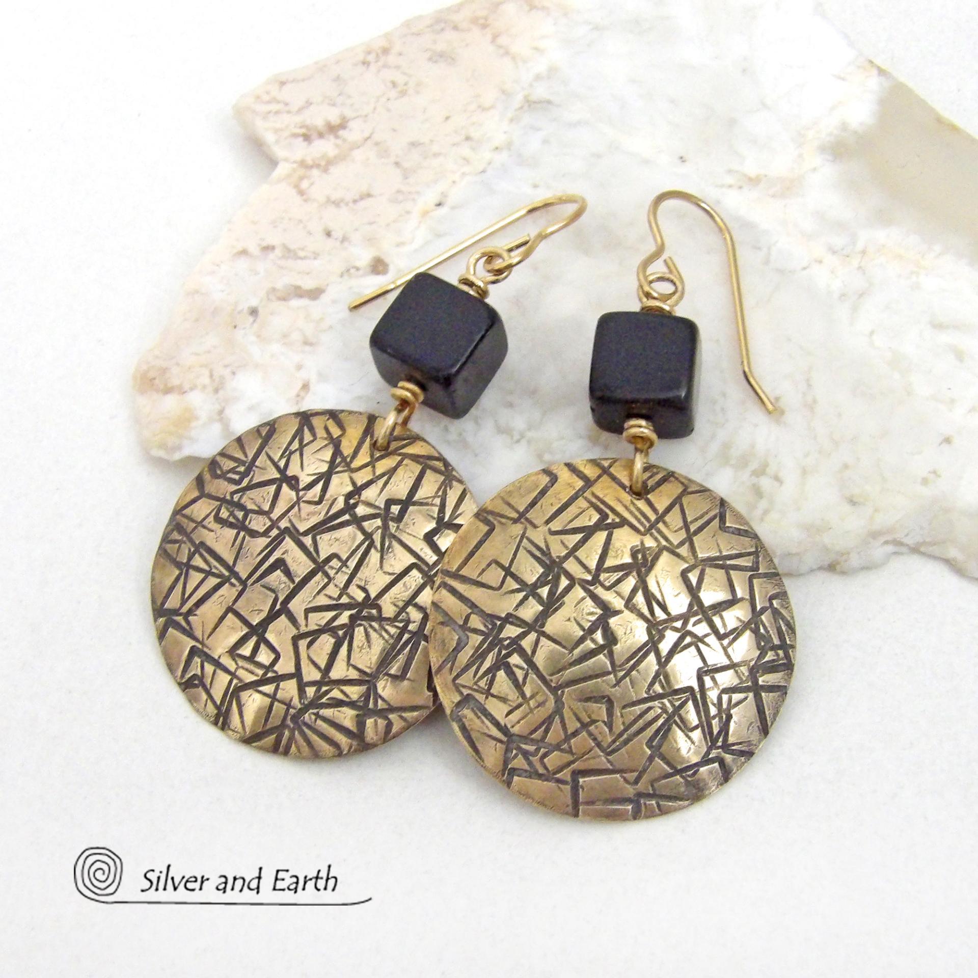 Artisan handcrafted round gold brass earrings with a hand-stamped abstract texture accented with cube-shaped matte black jasper stones on top. They have a modern contemporary vibe that coordinates beautifully with all wardrobe styles.