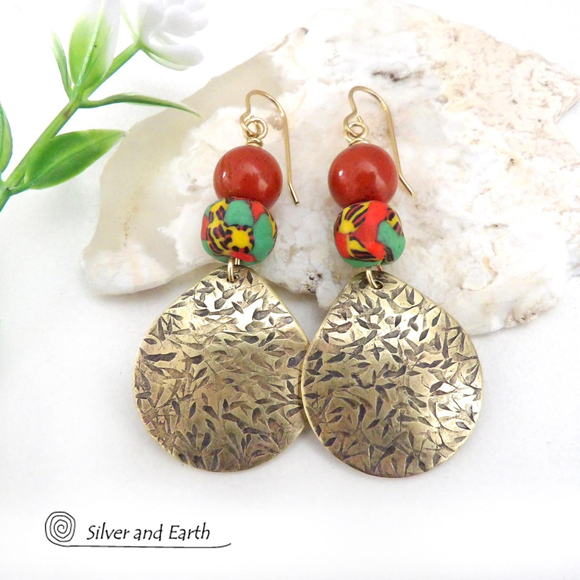 These handcrafted earrings feature gold brass dangles with a hand textured design accented with red jasper gemstones and colorful African glass beads with multi-colored hues of green, red, yellow and black. They have a bold exotic, tribal vibe with a vibrant pop of color that makes a unique statement.