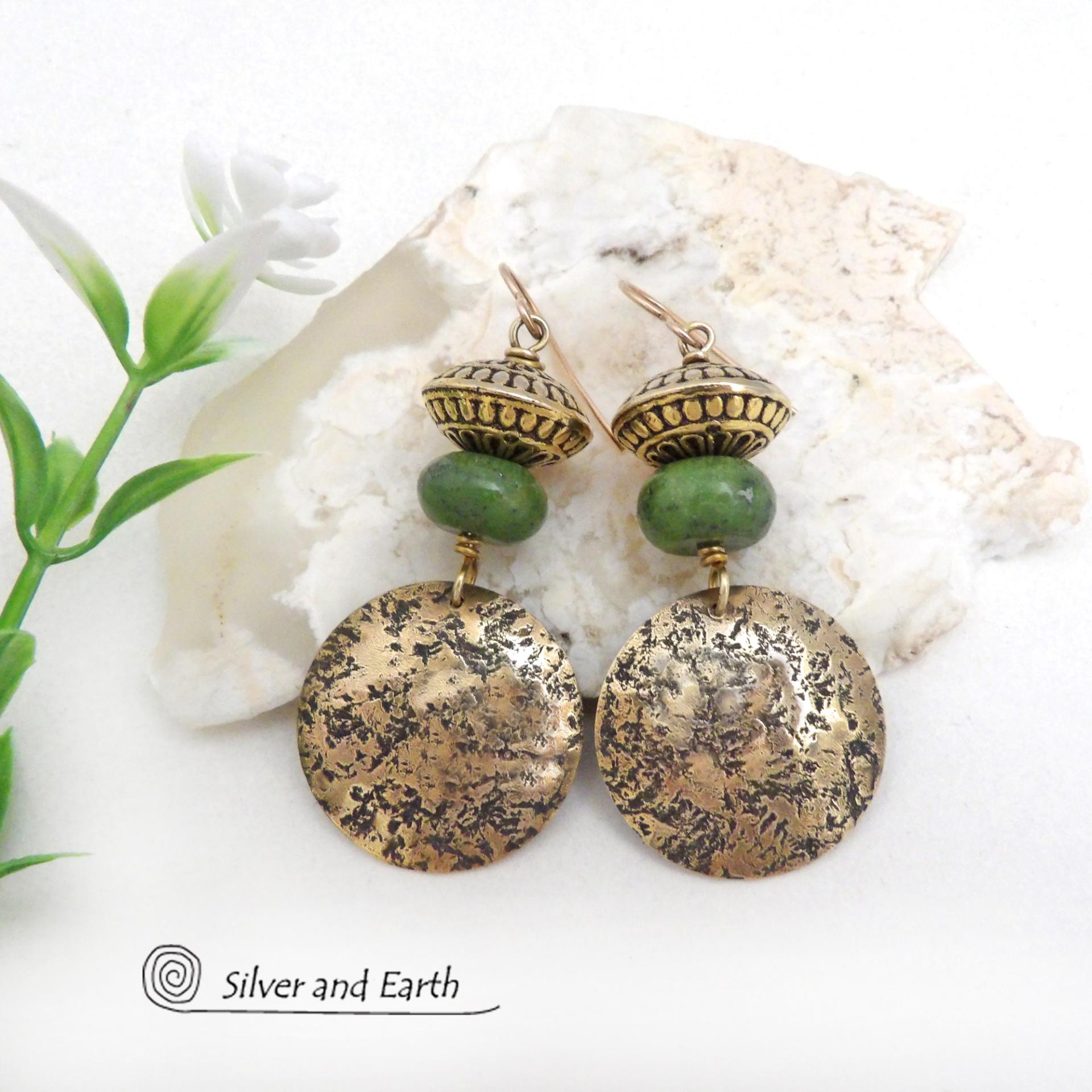 These handcrafted earrings feature round gold brass dangles with a lightly hammered organic texture accented with natural green serpentine gemstones and textured brass beads. They have an earthy elegant and modern style that coordinates beautifully with all wardrobe styles. Perfect for your spring wardrobe - or any time of year.These handcrafted earrings showcase a unique blend of textures and patterns, perfect for adding a touch of bohemian style to any outfit. 