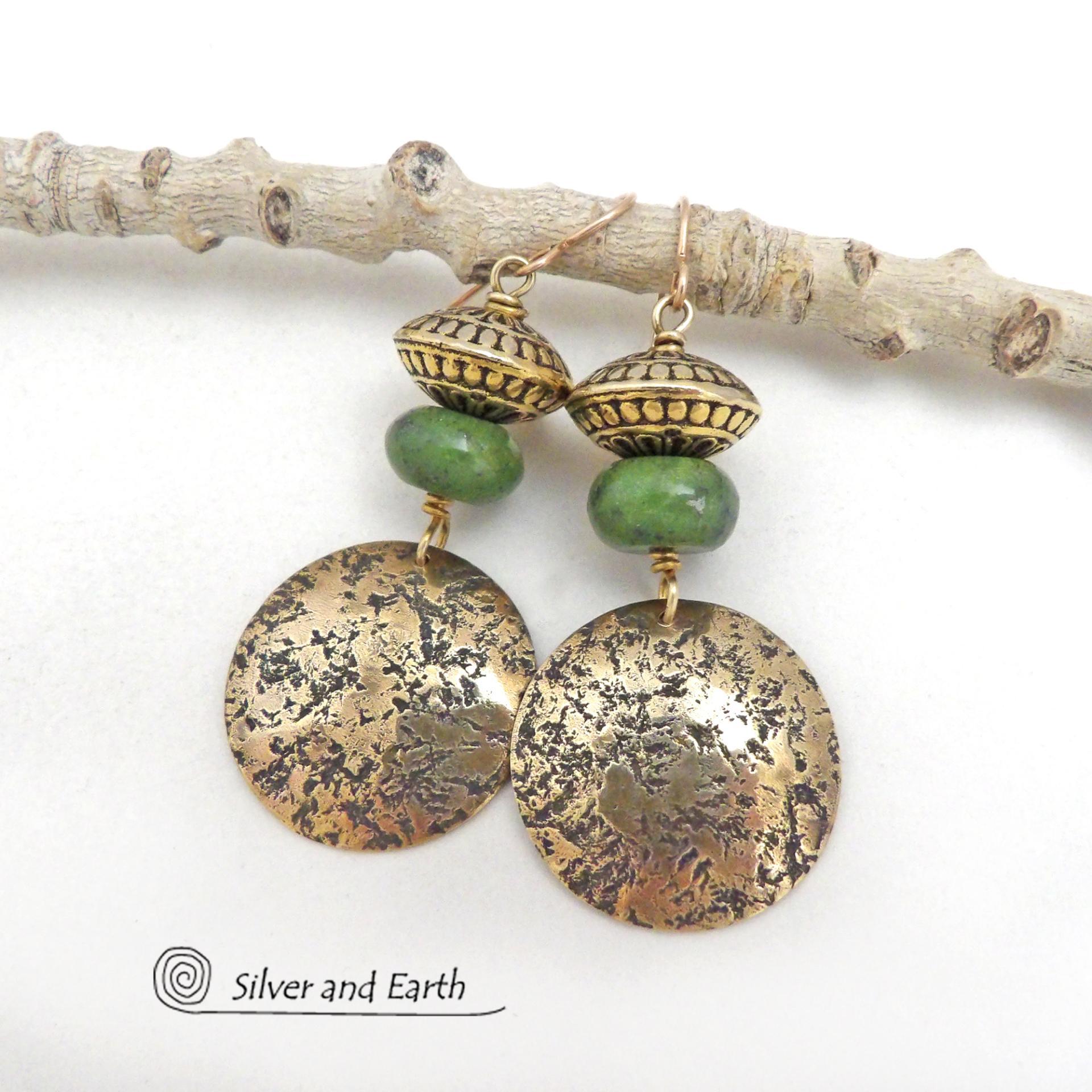 These handcrafted earrings feature round gold brass dangles with a lightly hammered organic texture accented with natural green serpentine gemstones and textured brass beads. They have an earthy elegant and modern style that coordinates beautifully with all wardrobe styles. Perfect for your spring wardrobe - or any time of year. These handcrafted earrings showcase a unique blend of textures and patterns, perfect for adding a touch of bohemian style to any outfit.