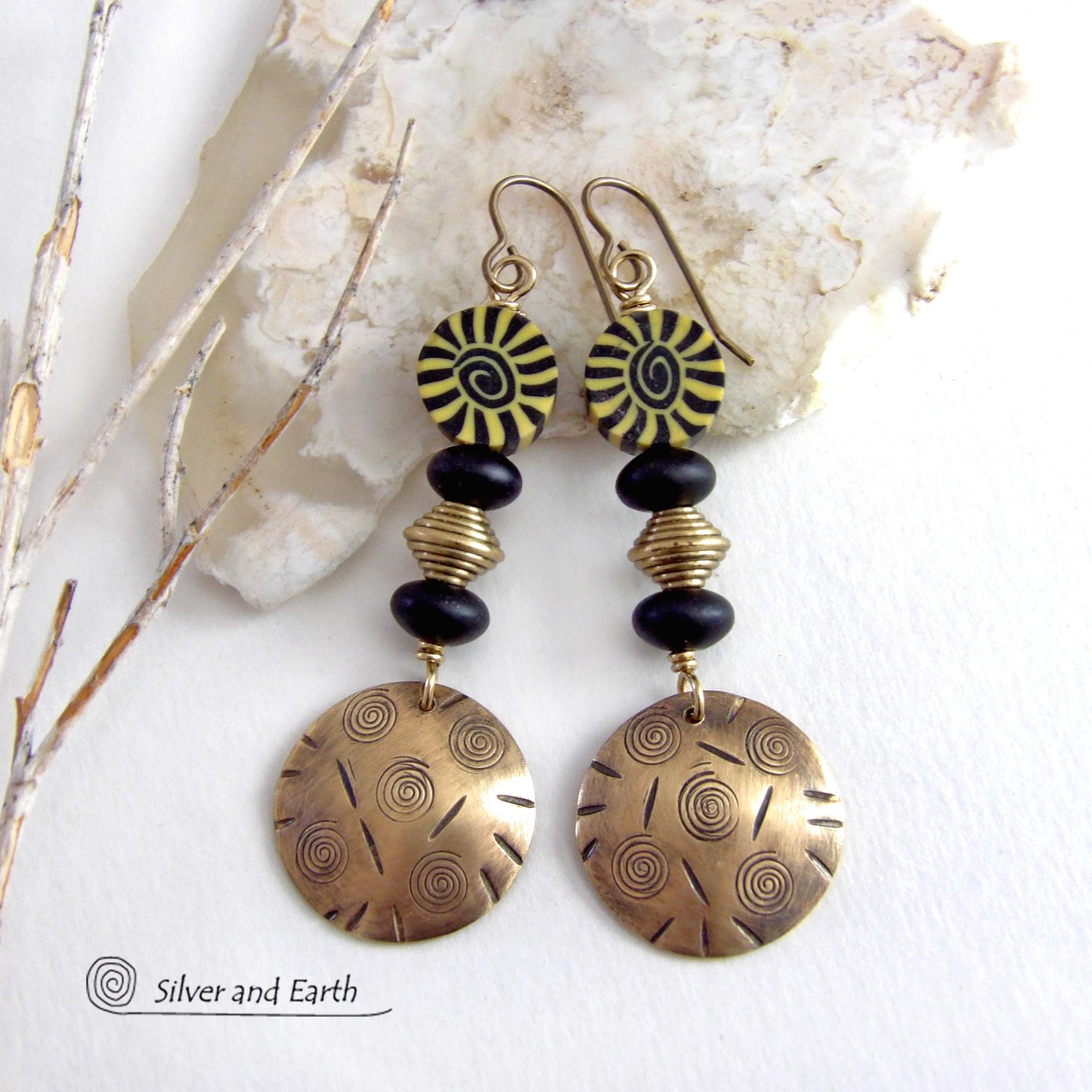 These handcrafted earrings have an ethnic boho tribal vibe. They feature gold brass dangles with a hand stamped spiral and line texture accented with black and light yellow Fimo clay beads with a spiral design, black glass and brass beads. Unique and fun to wear - they have a funky bohemian vibe that makes a bold, striking statement. Perfect for women that love to wear one-of-a-kind artisan handcrafted jewelry. Handmade in the USA by Silver and Earth Jewelry. 