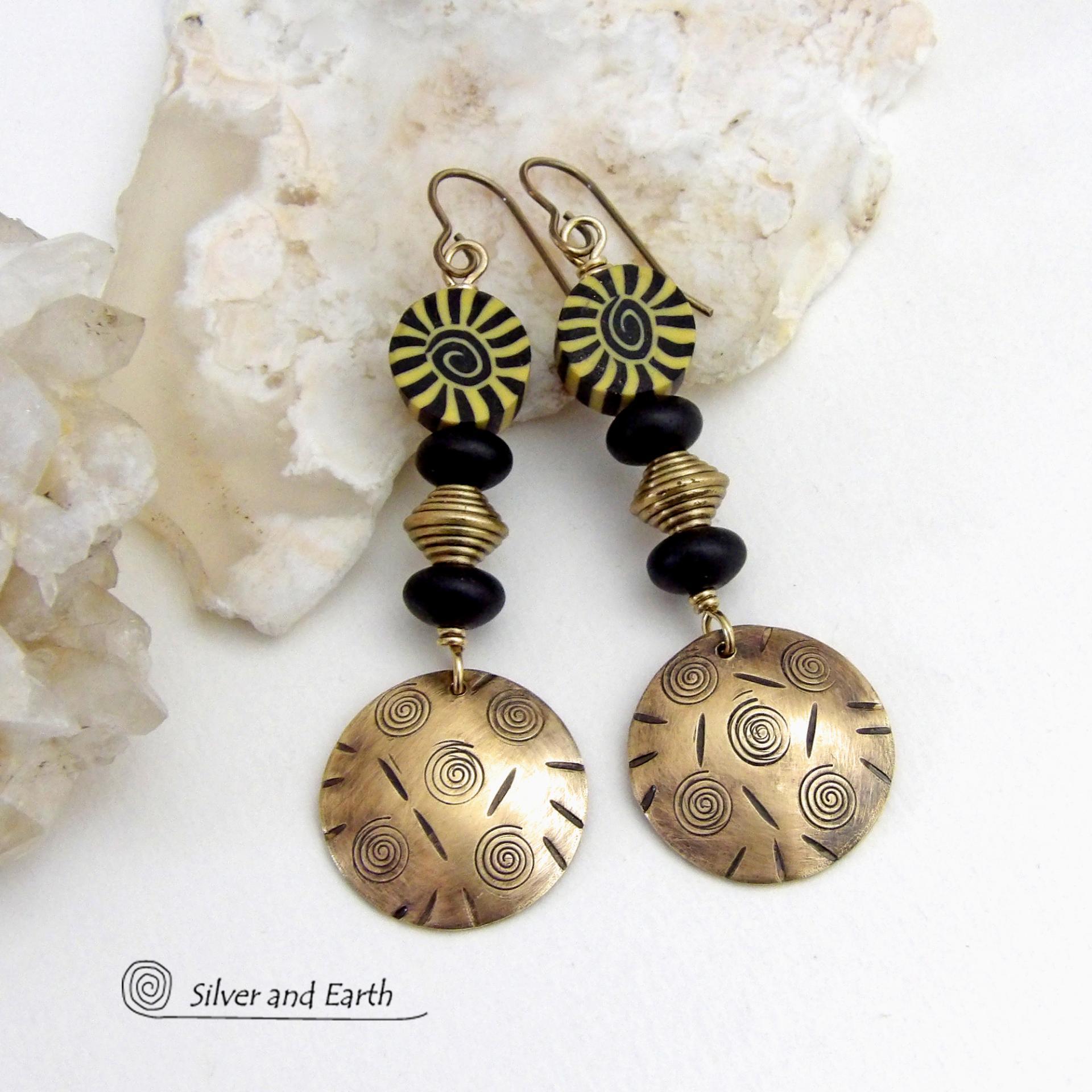 These handcrafted earrings have an ethnic boho tribal vibe. They feature gold brass dangles with a hand stamped spiral and line texture accented with black and light yellow Fimo clay beads with a spiral design, black glass and brass beads. Unique and fun to wear - they have a funky bohemian vibe that makes a bold, striking statement. Perfect for women that love to wear one-of-a-kind artisan handcrafted jewelry. Handmade in the USA by Silver and Earth Jewelry. 