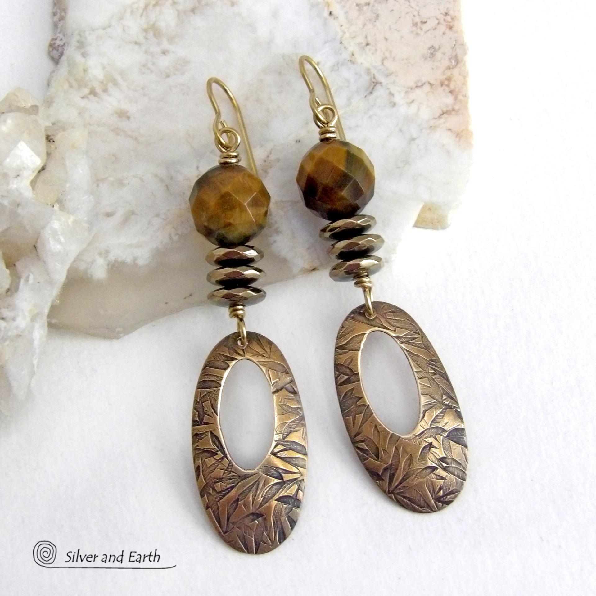 These handcrafted earrings feature gold brass oval hoop dangles with a hand stamped texture accented with natural brown tiger's eye gemstones and faceted hematite stones with an electroplated champagne gold finish. The stones have a beautiful brown hue with undertones of gold and a faceted finish which casts off a natural sparkle and shine. They have a modern, chic and elegant style that coordinates beautifully with all wardrobe types - dressed up or down.