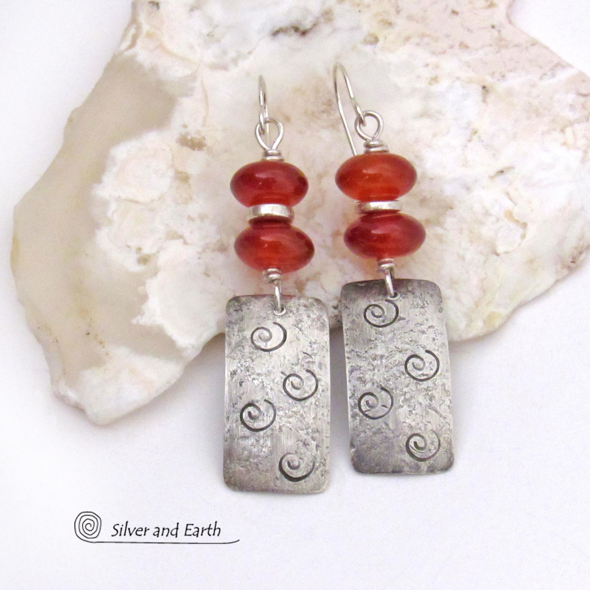 These handcrafted sterling silver earrings are accented with a stack of natural carnelian gemstones with a rusty orange hue and tiny silver pewter spacer beads. The silver dangles have a hand stamped spiral pattern and a lightly hammered background texture. Unique and fun to wear - they have an earthy, modern style with a touch of boho flair.
