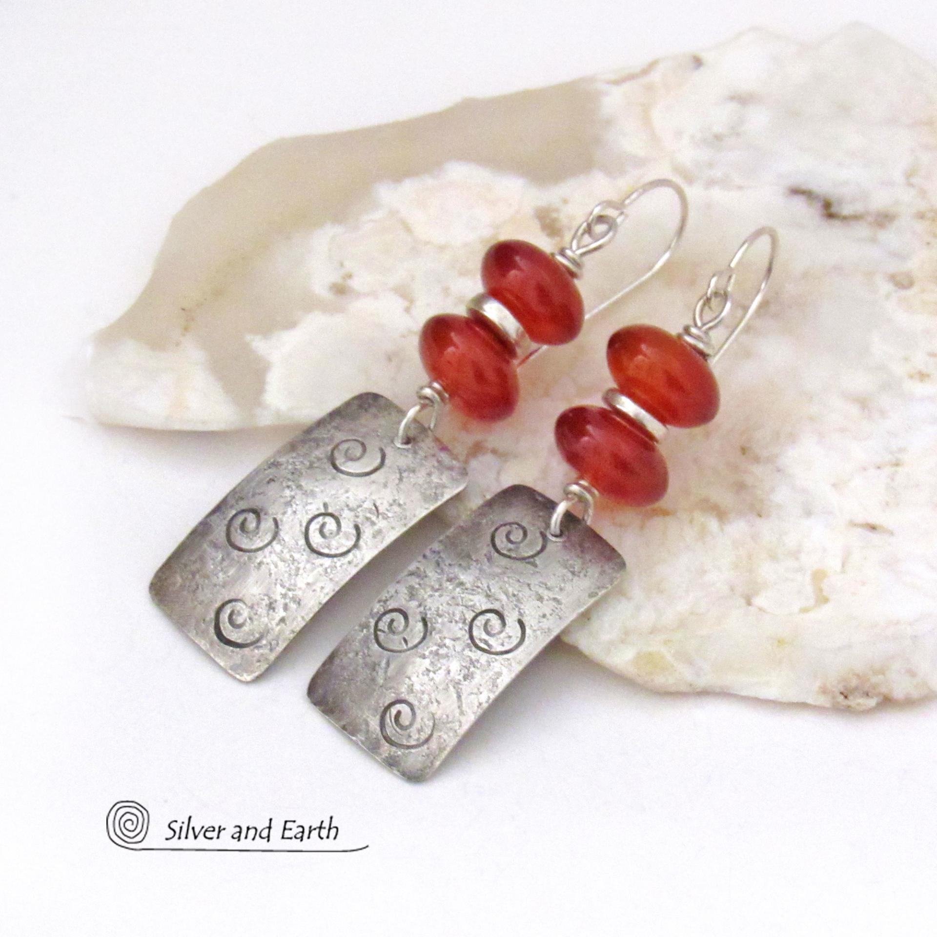 These handcrafted sterling silver earrings are accented with a stack of natural carnelian gemstones with a rusty orange hue and tiny silver pewter spacer beads. The silver dangles have a hand stamped spiral pattern and a lightly hammered background texture. Unique and fun to wear - they have an earthy, modern style with a touch of boho flair.
