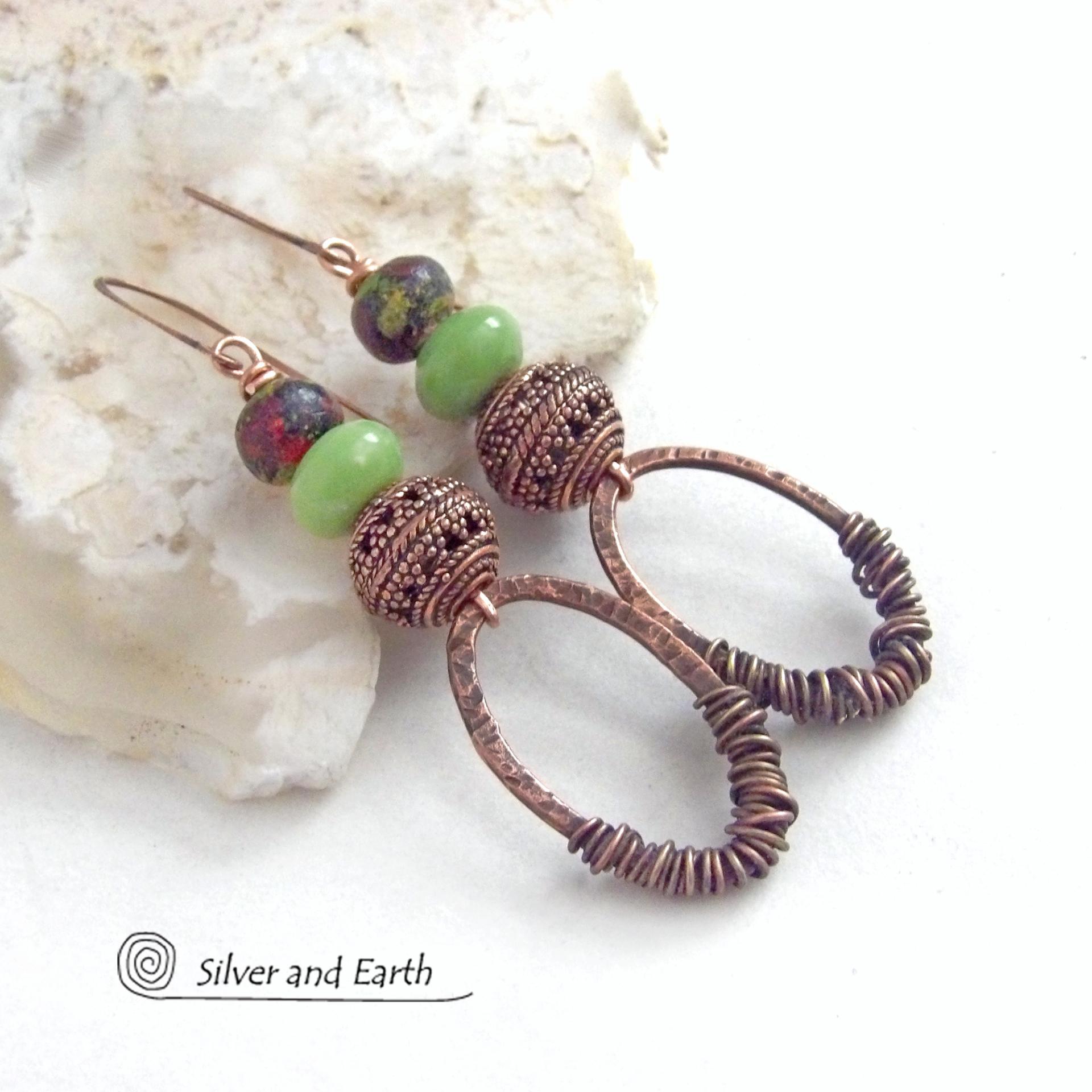 These handmade earrings feature wire wrapped copper oval hoops accented with copper filigree beads, green serpentine gemstones and hand painted wood beads. They have a bold exotic vibe with an ethnic tribal flair and are sure to make a unique statement.