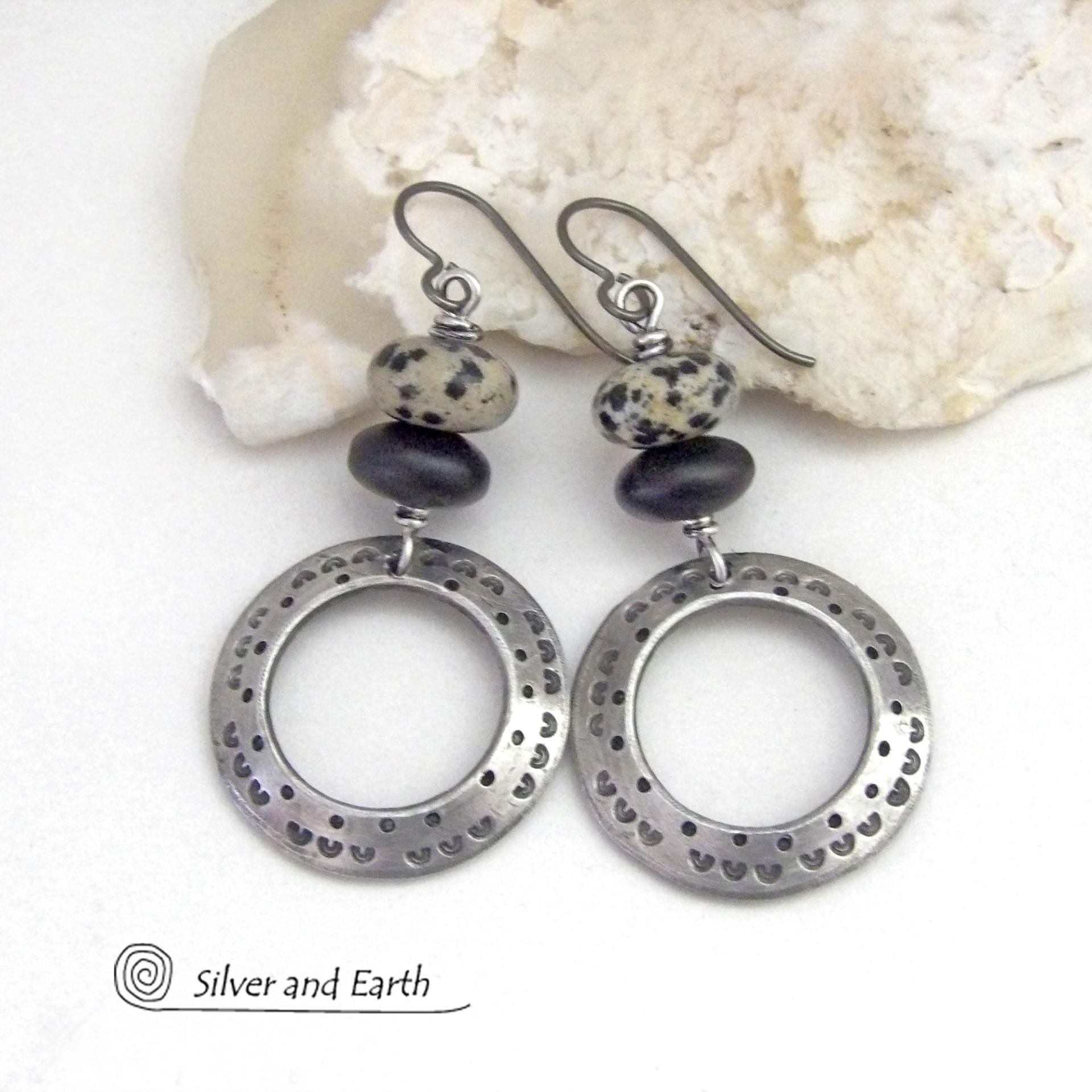 These handcrafted silver pewter hoop earrings have a hand stamped texture accented with natural dalmatian jasper gemstones and matte black glass beads. This type of jasper is known for its spotted pattern that resembles the Dalmatian breed of dog. These earrings have a modern, earthy boho chic style that coordinates beautifully with all wardrobe styles. Handmade the USA by Silver and Earth Jewelry.