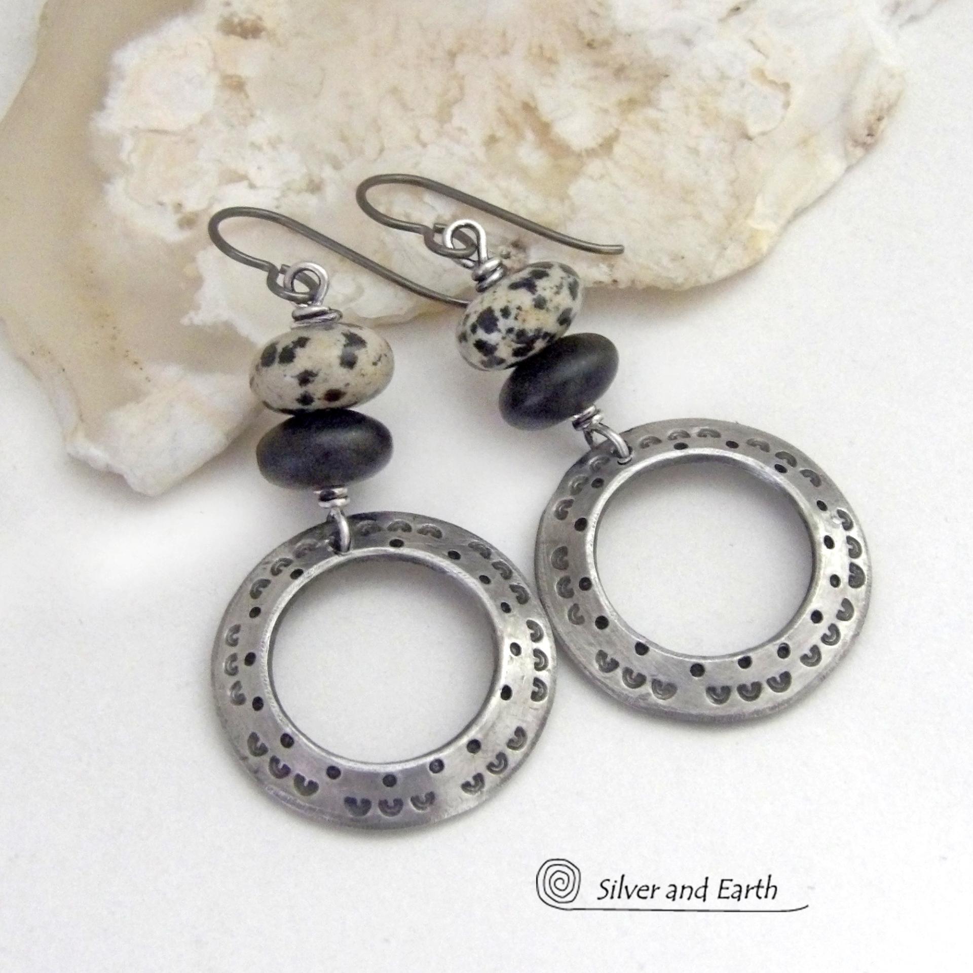 These handcrafted silver pewter hoop earrings have a hand stamped texture accented with natural dalmatian jasper gemstones and matte black glass beads. This type of jasper is known for its spotted pattern that resembles the Dalmatian breed of dog. These earrings have a modern, earthy boho chic style that coordinates beautifully with all wardrobe styles. Handmade the USA by Silver and Earth Jewelry.