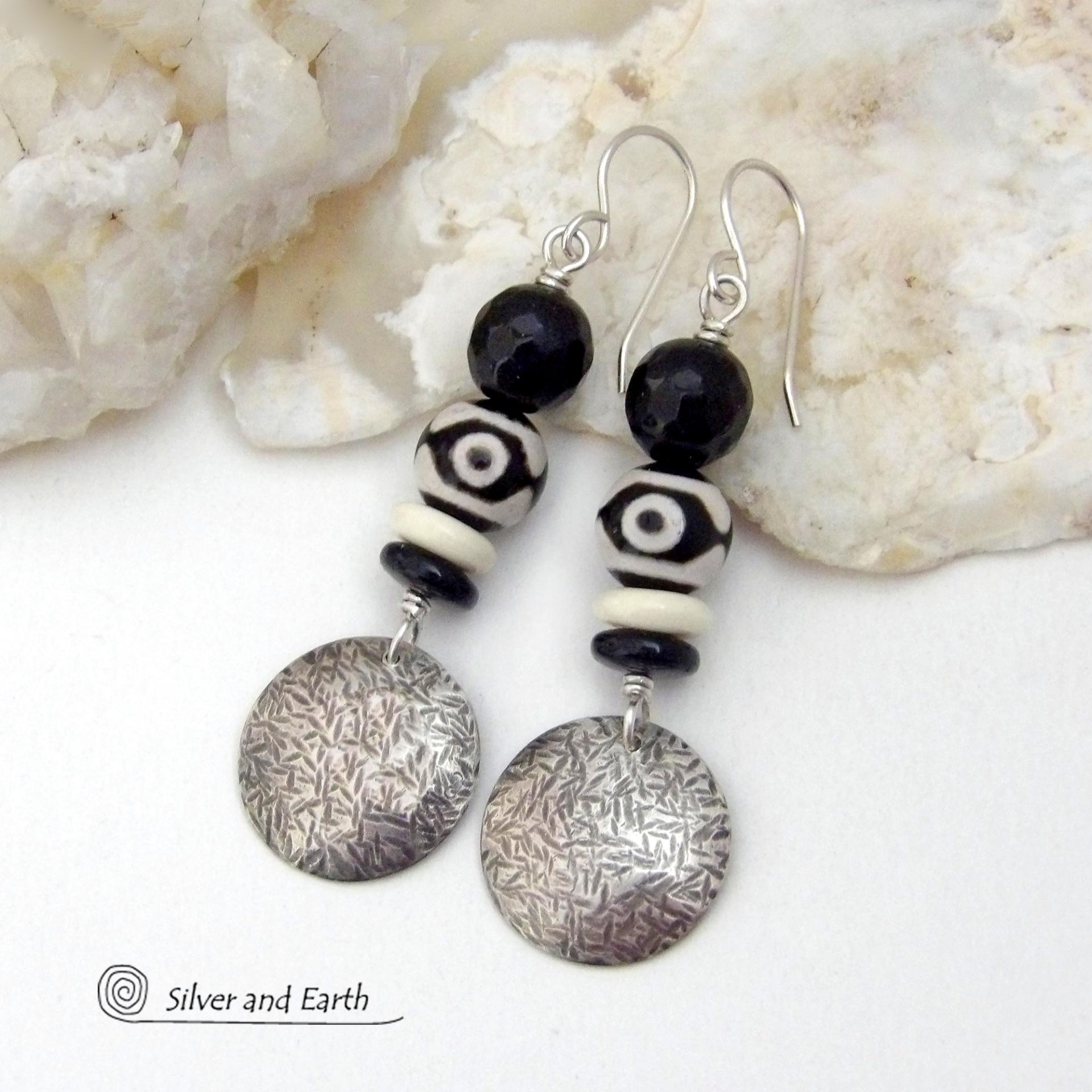 These earrings have a modern style with an ethnic tribal vibe. They feature handcrafted sterling silver circle dangles with a hammered texture accented with black and white Tibetan eye agate gemstones, onyx and bone beads, topped off with round black onyx gemstones with a faceted finish. Unique and striking, they'll make a bold statement. 