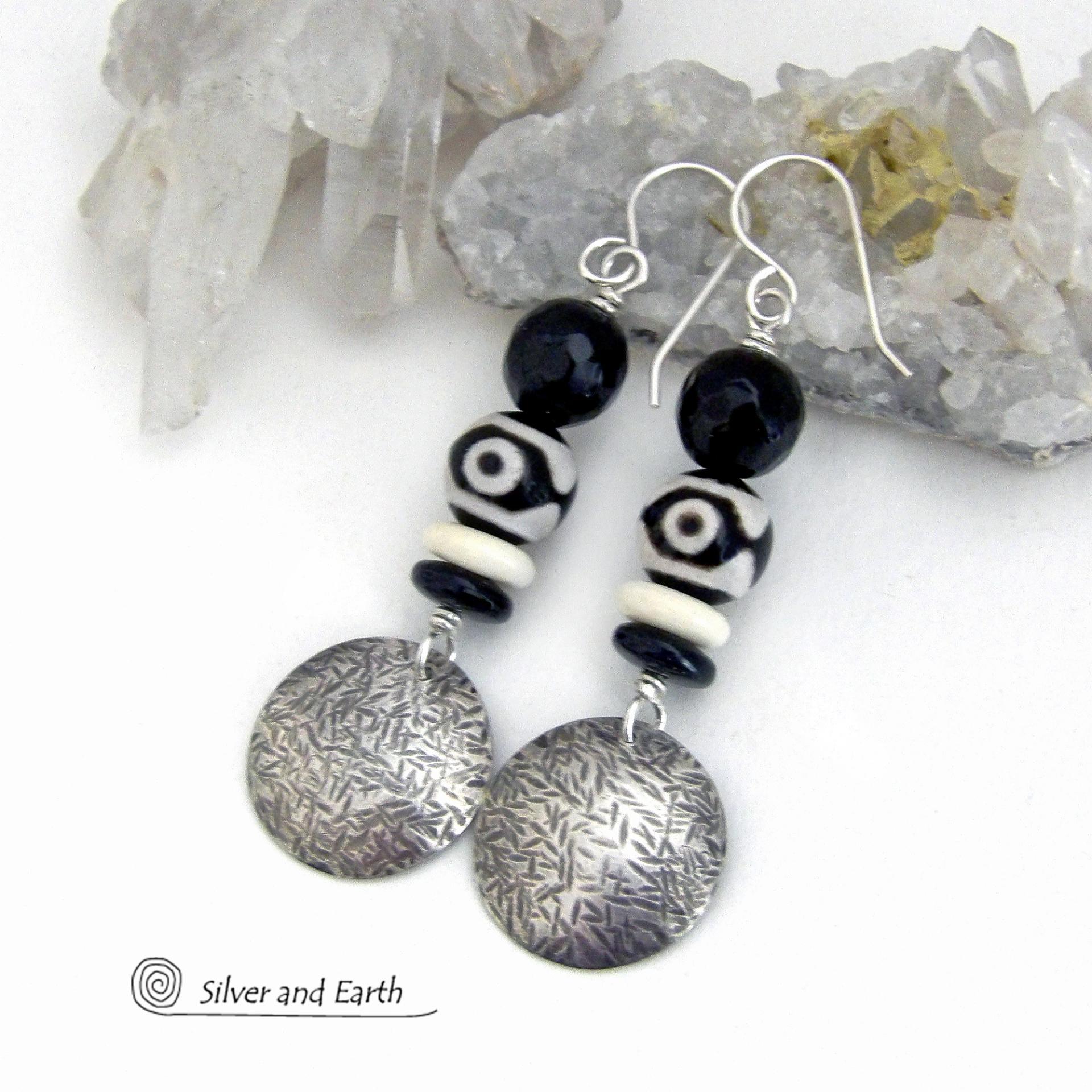 These earrings have a modern style with an ethnic tribal vibe. They feature handcrafted sterling silver circle dangles with a hammered texture accented with black and white Tibetan eye agate gemstones, onyx and bone beads, topped off with round black onyx gemstones with a faceted finish. Unique and striking, they'll make a bold statement. 