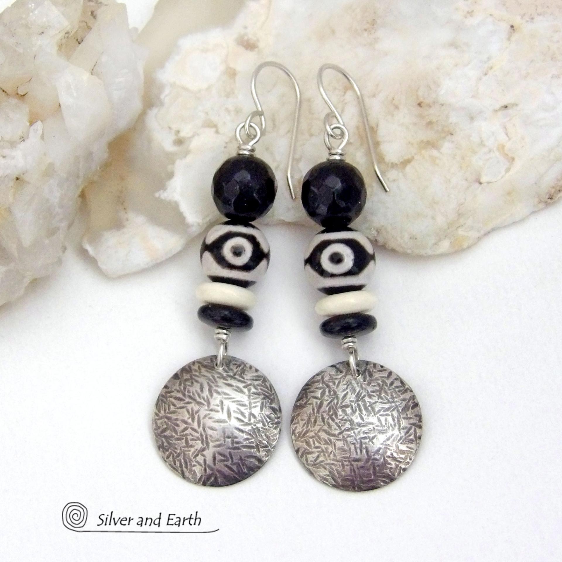 These earrings have a modern style with an ethnic tribal vibe. They feature handcrafted sterling silver circle dangles with a hammered texture accented with black and white Tibetan eye agate gemstones, onyx and bone beads, topped off with round black onyx gemstones with a faceted finish. Unique and striking, they'll make a bold statement. 