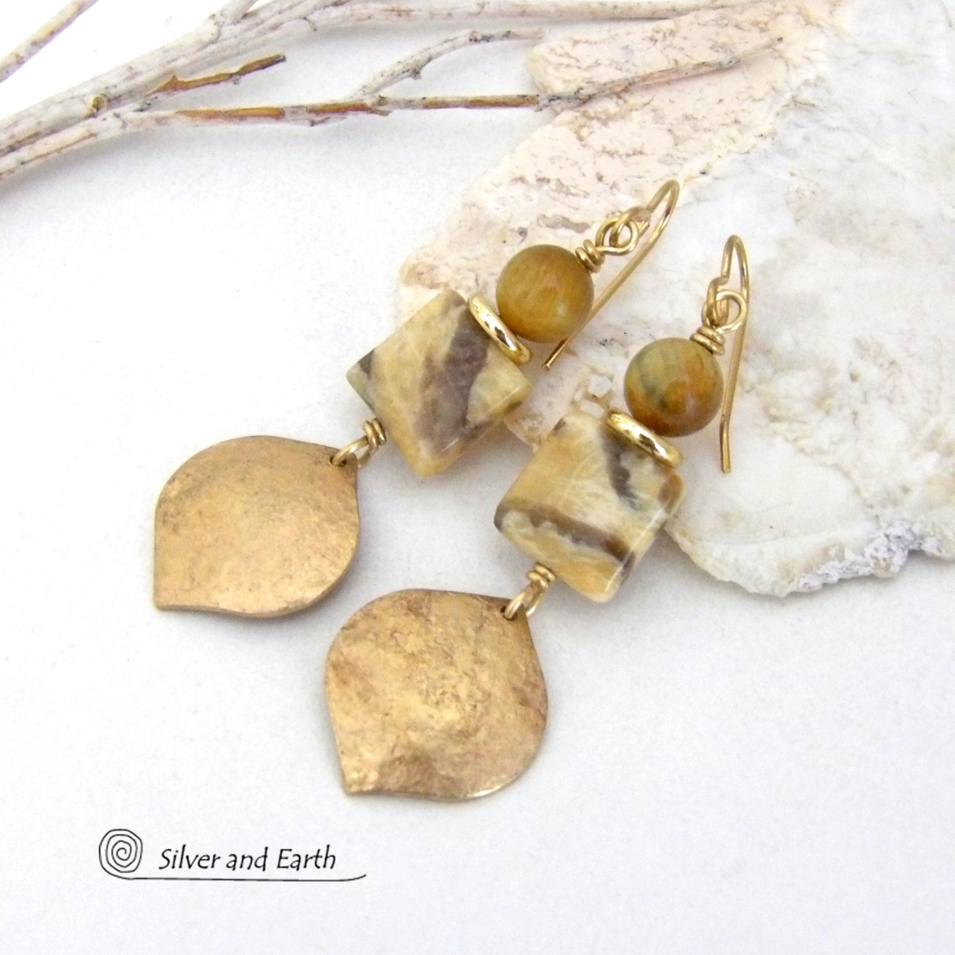 Unique and one-of-a-kind, these artisan handcrafted earrings feature shiny gold brass dangles with a hammered raw silk texture accented with graphic feldspar and golden tiger's eye gemstones and shiny brass beads. Graphic feldspar is a type of moonstone that has smoky quartz inclusions which creates unique natural patterns. They have an elegant, modern chic style that looks great dressed up or down. 