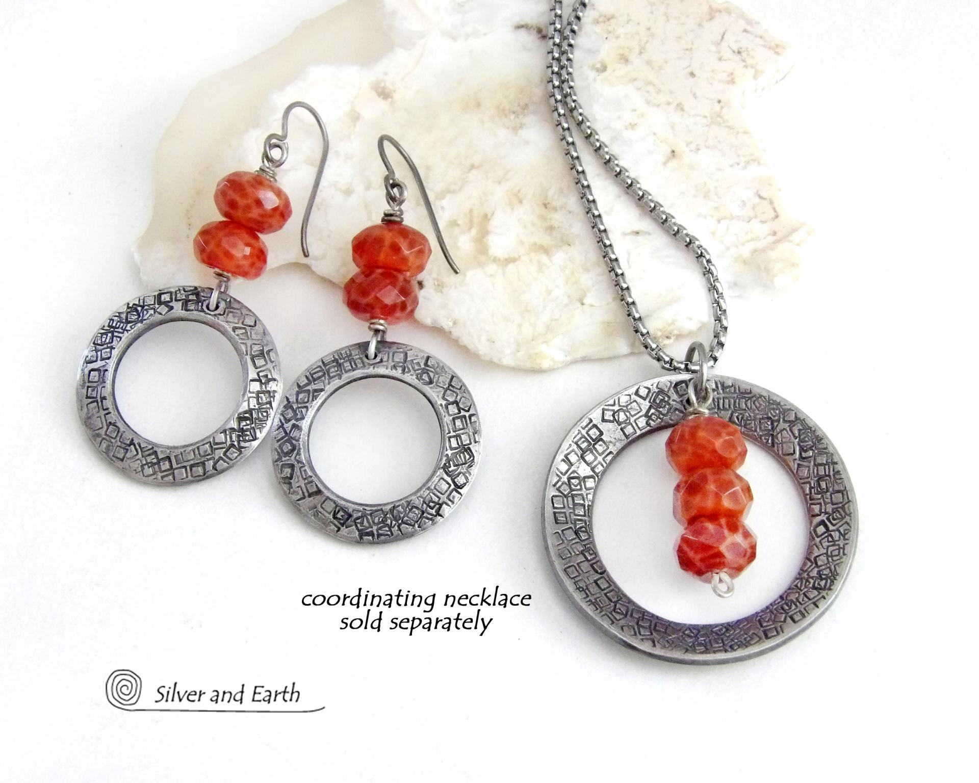 These handcrafted earrings feature silver tone pewter hoops with a hand stamped texture accented with a stack of orange fire agate gemstones. Matching necklace sold separately. 
