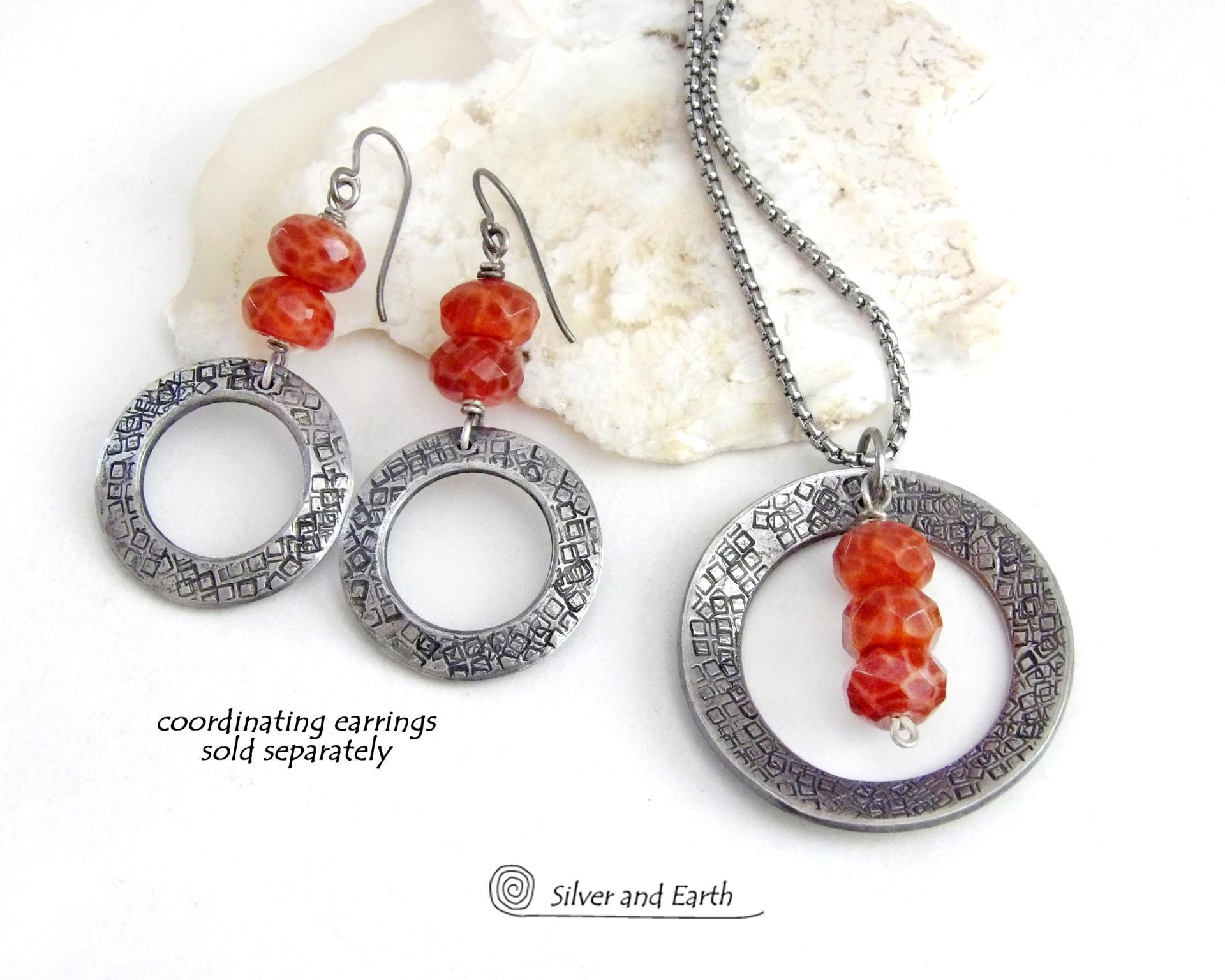 This handcrafted pendant necklace features a silver tone pewter circle with a hand stamped texture accented with a stack of faceted orange fire agate gemstones that dangle in front. It has a classic, earthy modern style that coordinates well with all wardrobe types. Matching earrings sold separately.