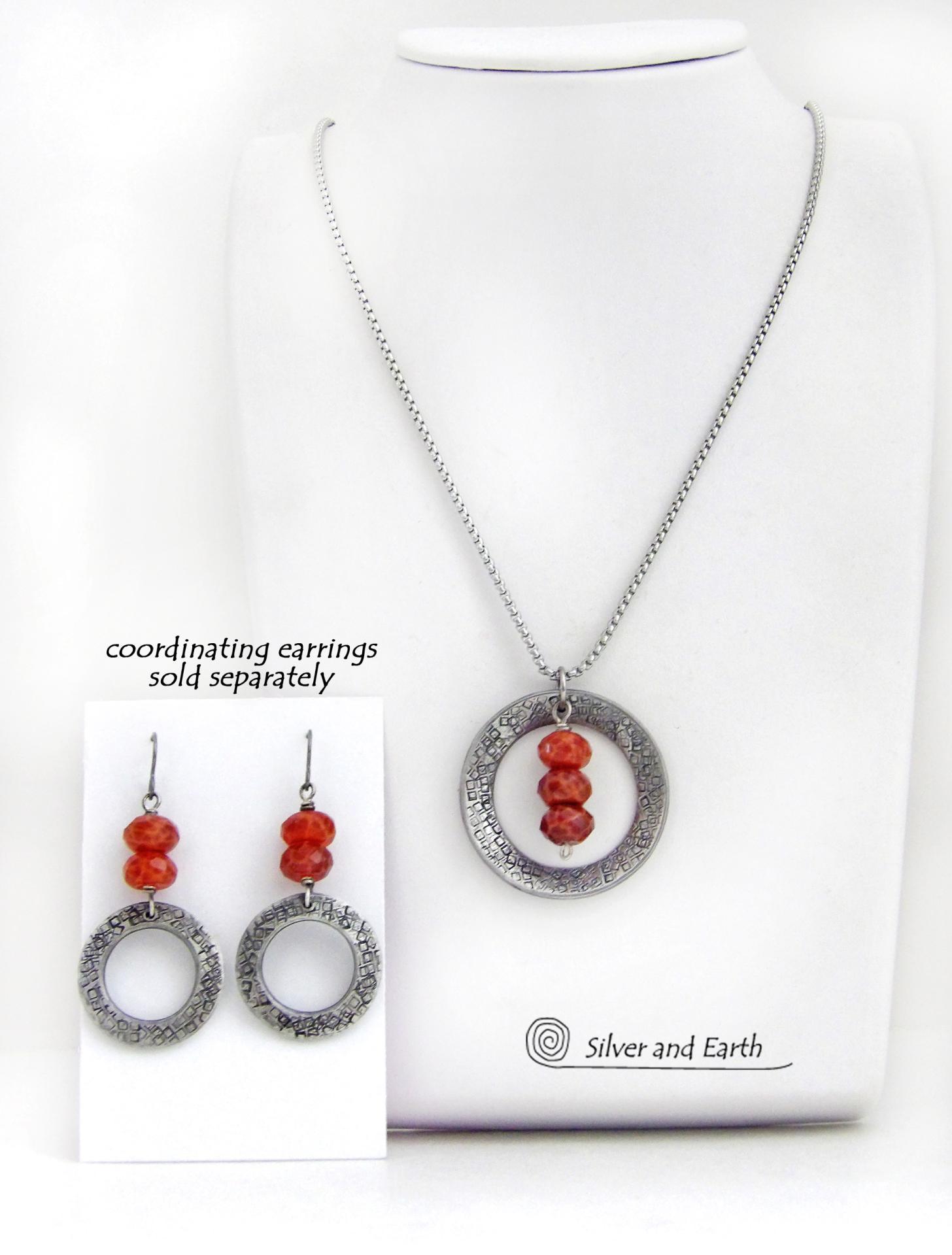This handcrafted pendant necklace features a silver tone pewter circle with a hand stamped texture accented with a stack of faceted orange fire agate gemstones that dangle in front. It has a classic, earthy modern style that coordinates well with all wardrobe types. Matching earrings sold separately.