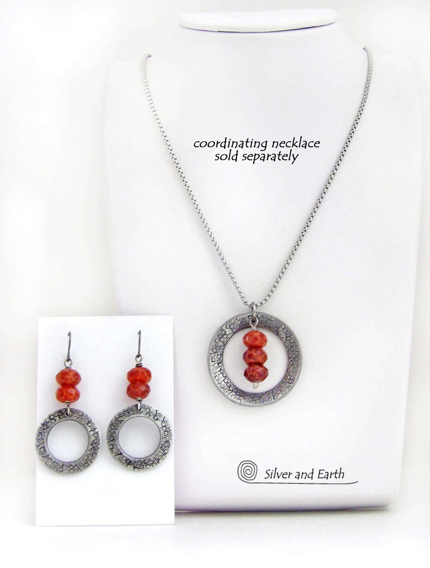 These handcrafted earrings feature silver tone pewter hoops with a hand stamped texture accented with a stack of orange fire agate gemstones. Matching necklace sold separately. 