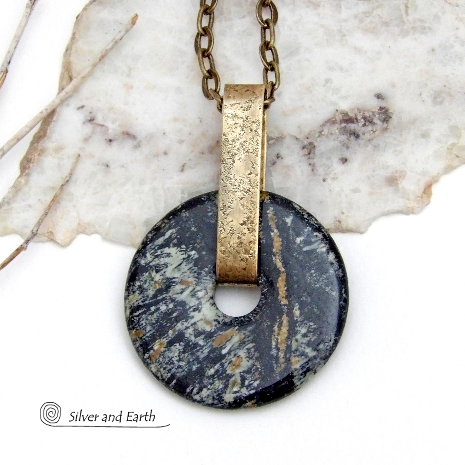 This one-of-a-kind pendant necklace has a large stunning fireworks jasper stone accented with a hand forged gold brass bail. The stone has a natural bold dramatic pattern in hues of black, gold, mint green and cream. The design is modern and bold - yet classic and always in fashion. It can be worn by either a man or women. It's reversible and can be worn on either side. (See all photos for alternate sides). Makes a great gift for a natural stone lover. Comes on a 18" antiqued gold brass chain necklace.