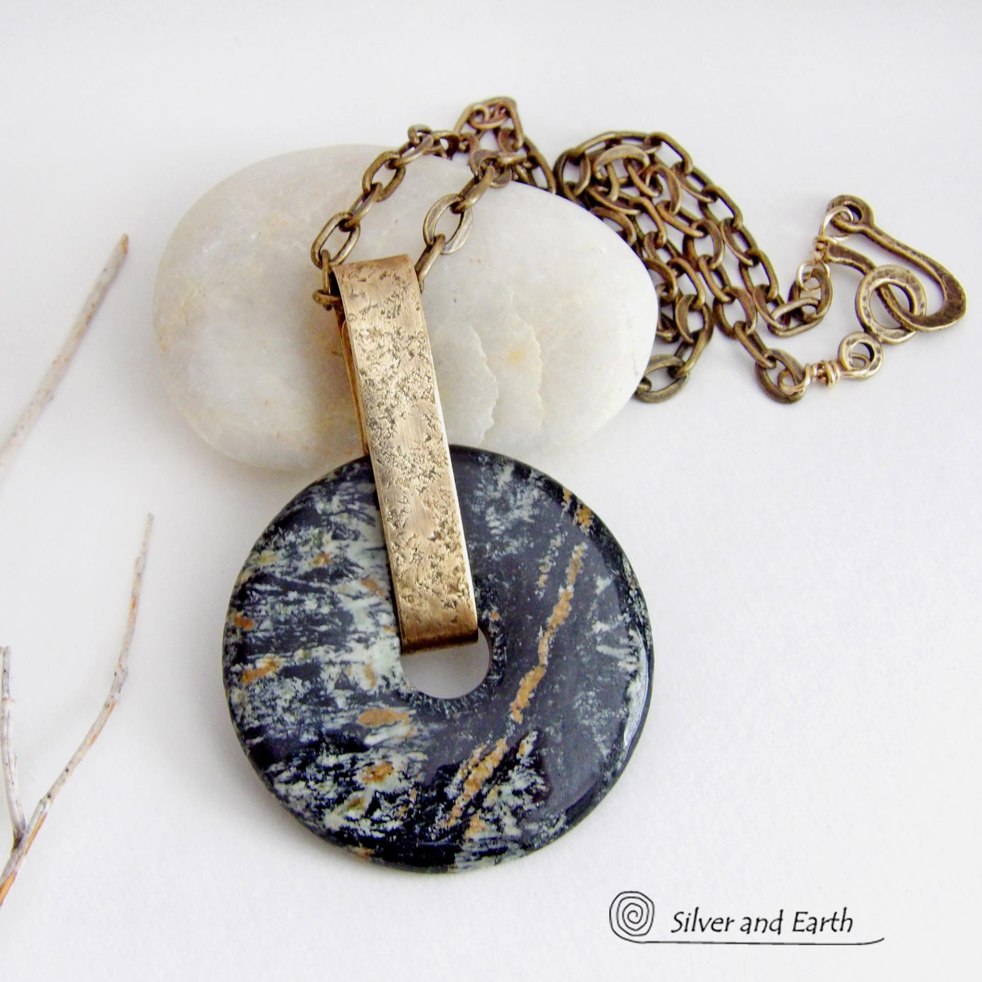 This one-of-a-kind pendant necklace has a large stunning fireworks jasper stone accented with a hand forged gold brass bail. The stone has a natural bold dramatic pattern in hues of black, gold, mint green and cream. The design is modern and bold - yet classic and always in fashion. It can be worn by either a man or women. It's reversible and can be worn on either side. Makes a great gift for a natural stone lover. It comes on a 18" antiqued gold brass chain necklace with lobster claw closure.