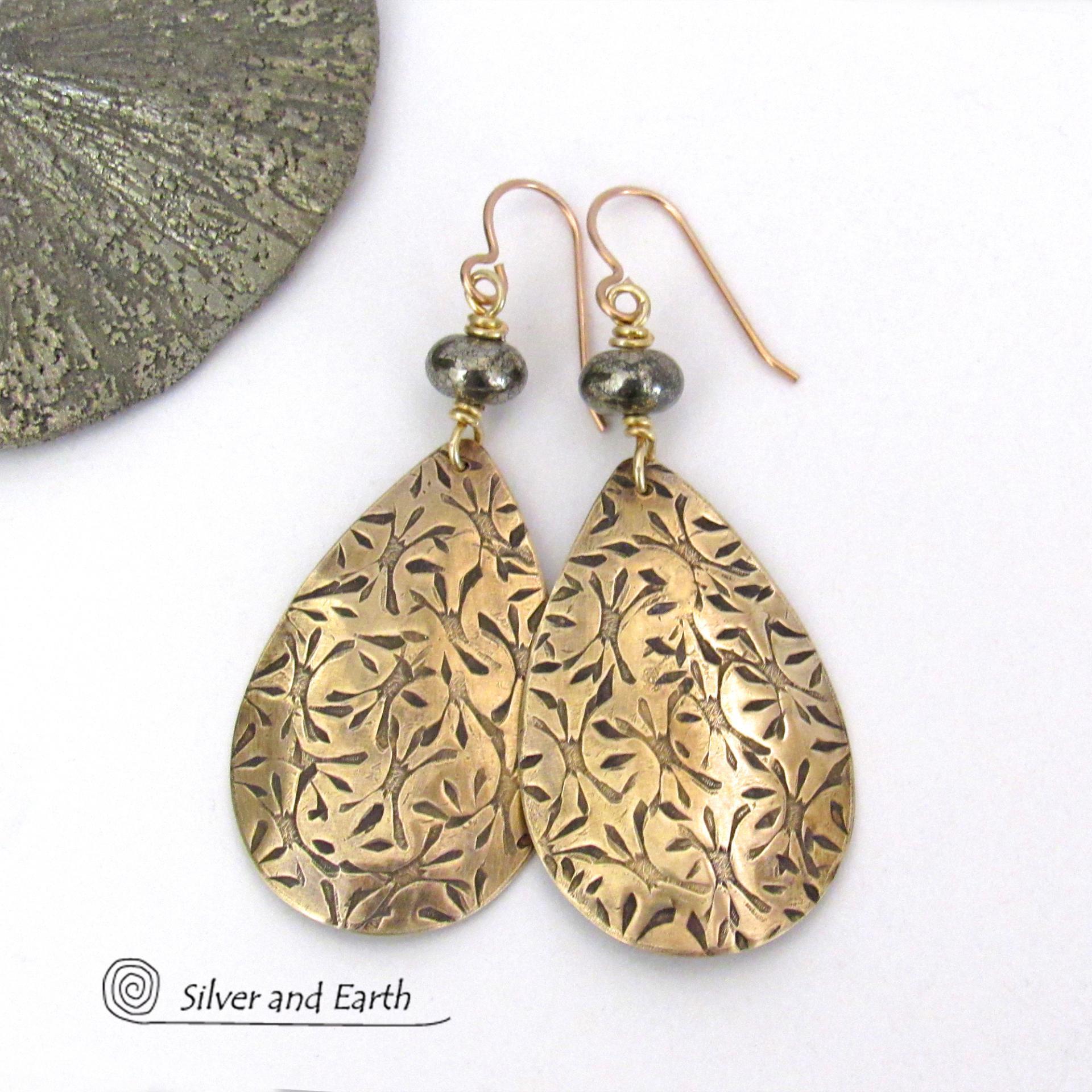 These handcrafted gold brass teardrop earrings have a hand stamped texture and are accented with natural silver pyrite gemstone beads. They have a modern contemporary style that coordinates beautifully with all wardrobe types.  MEASUREMENTS: Total length: 2-3/8” from top of bronze ear wires and 1” at widest point. Created out of solid gold brass; the shapes were hand stamped for texture; oxidized to enhance the detail. Handmade in the USA by Silver and Earth Jewelry.
