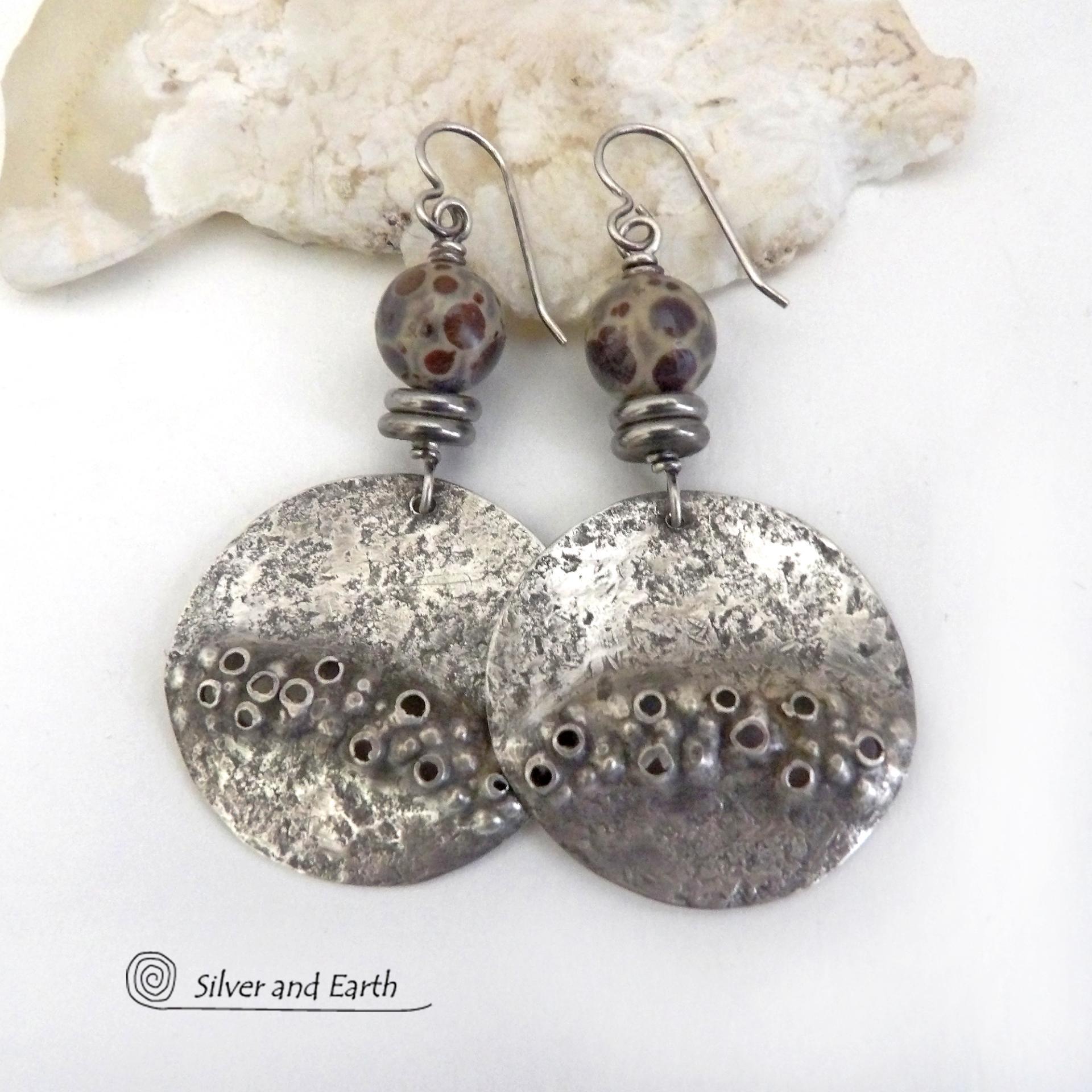 Unique and one-of-a-kind, these handcrafted large sterling silver earrings have a bold edgy vibe. They feature rustic hammered sterling silver accented with natural asteroid jasper stones and stainless steel beads. This type of stone is known for its unique dotted matrix in earth-tone hues of brown, gray and tan. It's also known as chocolate ocean jasper because it's found on the shores of Madagascar where ocean jasper is also found. Bold and exotic - they're sure to make a unique statement.