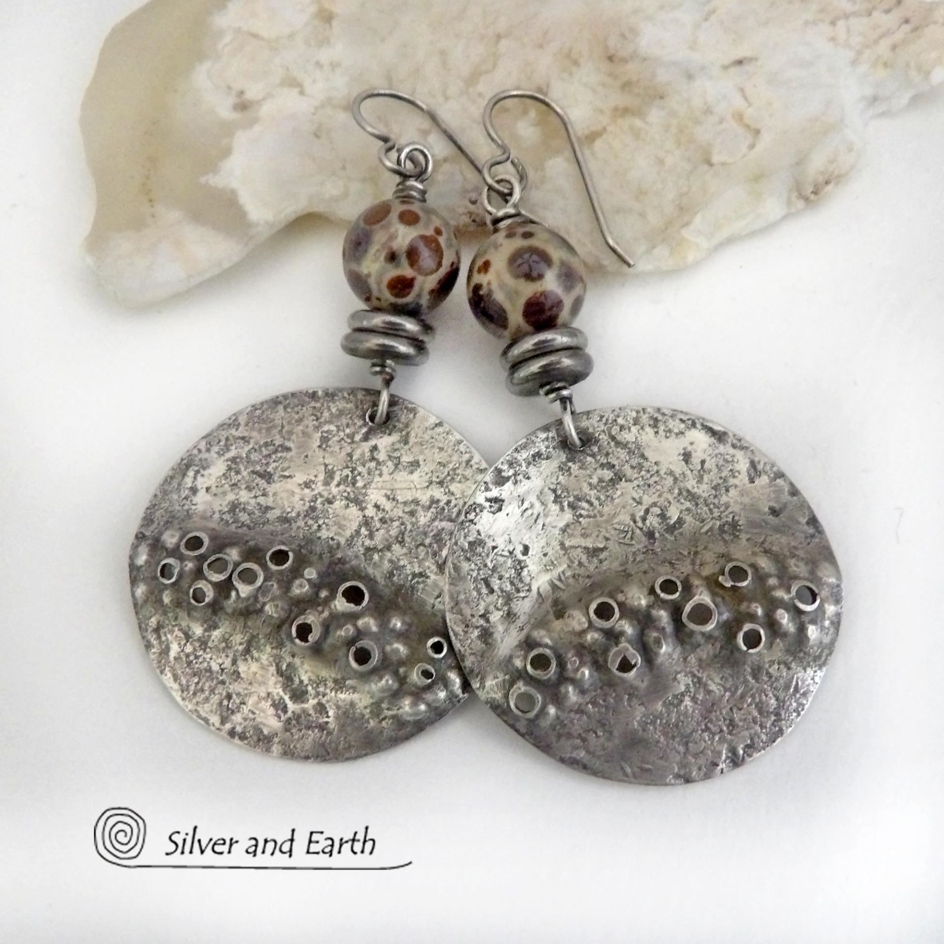 Unique and one-of-a-kind, these handcrafted large sterling silver earrings have a bold edgy vibe. They feature rustic hammered sterling silver accented with natural asteroid jasper stones and stainless steel beads. This type of stone is known for its unique dotted matrix in earth-tone hues of brown, gray and tan. It's also known as chocolate ocean jasper because it's found on the shores of Madagascar where ocean jasper is also found. Bold and striking - they're sure to make a unique statement.