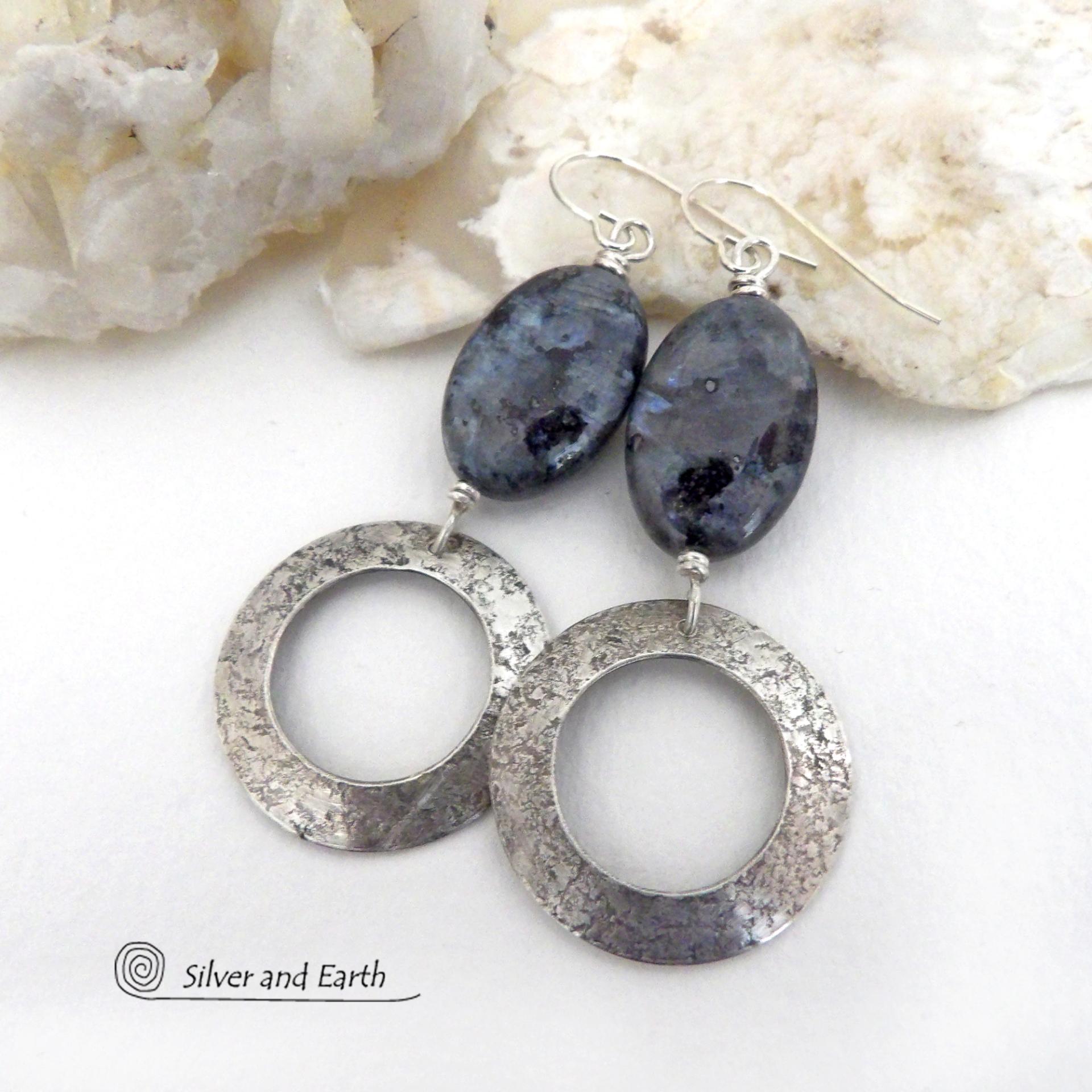 These handcrafted earrings feature natural larvikite gemstones accented with sterling silver hoop dangles with a lightly hammered texture. The stones have a pearly, grayish black hue - along with blue iridescent flashes of light which cast off a natural shimmer & shine. Perfect "go to" earrings that will look great with all wardrobe styles - dressed up or down! Larvikite originates from the Larvik region in Norway and is also called Norwegian moonstone and black labradorite.