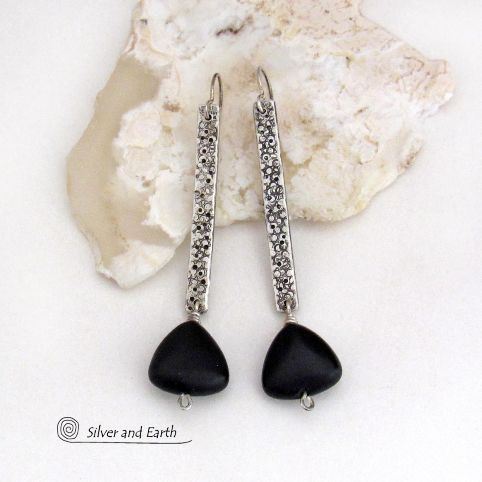These handcrafted earrings feature long textured skinny strips of sterling silver accented with triangular-shaped black onyx stones with a matte finish. They have a contemporary modern style with a bold, edgy vibe.