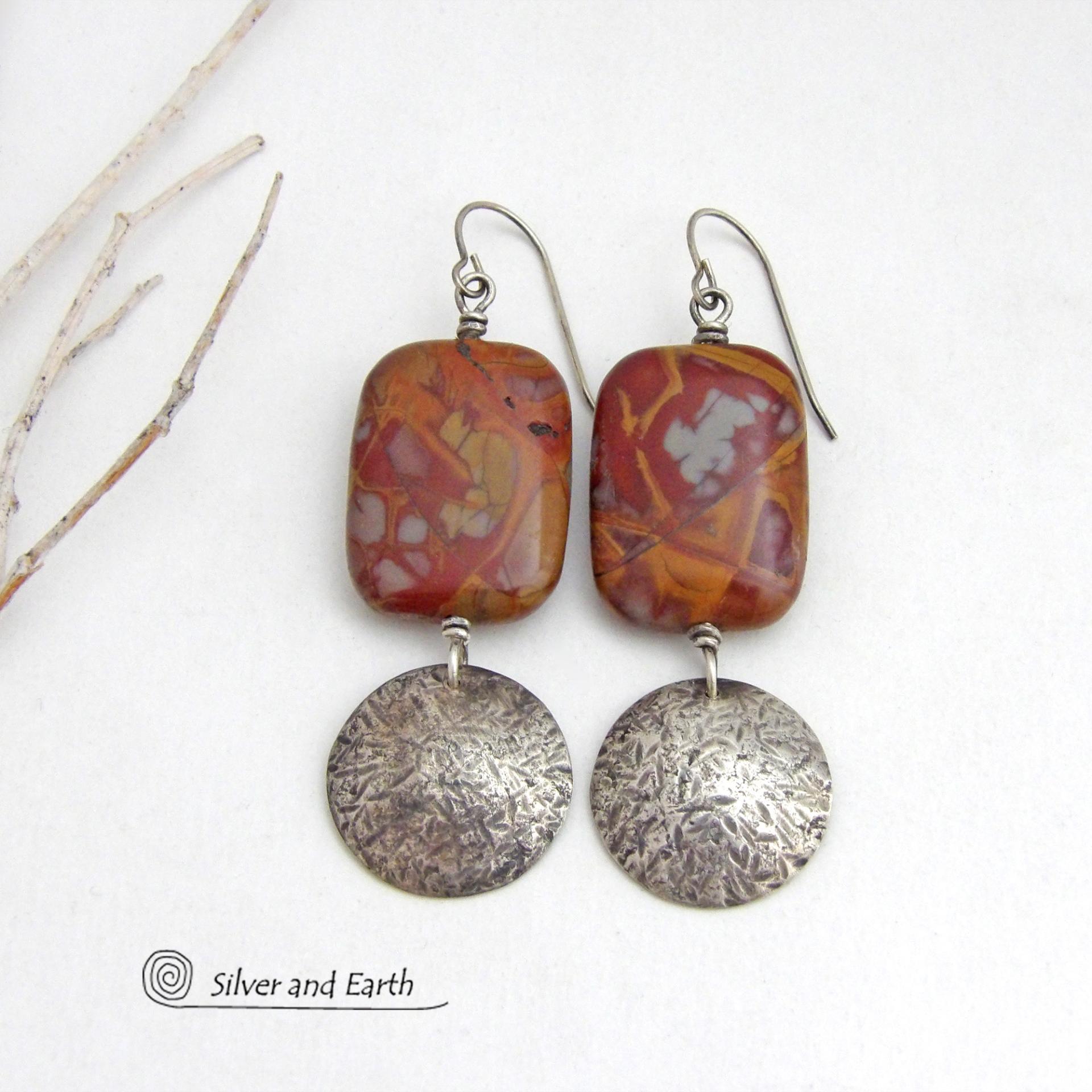 These one-of-a-kind handcrafted earrings feature natural Noreena jasper gemstones accented with textured sterling silver dangles. This stone is known for its dramatic abstract and geometric patterns and is found only in the Pilbara region of Western Australia. The stones in this pair have a great pattern consisting of hues of deep burgundy-red with fiery orange and gray streaks. 