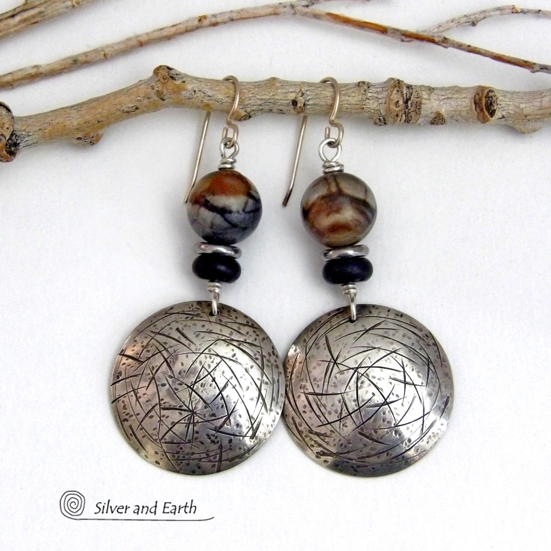 These one-of-a-kind earrings feature handcrafted sterling silver with a hammered and hand stamped texture accented with earthy natural Picasso marble gemstones, black glass and stainless steel beads. This semiprecious stone is found only in southwest Utah. It's named after the famous artist because the natural matrix of geometric lines resembles an abstract painting. The stones in this pair have a beautiful matrix pattern of distinctive swirly lines in black, grey and chocolate brown.