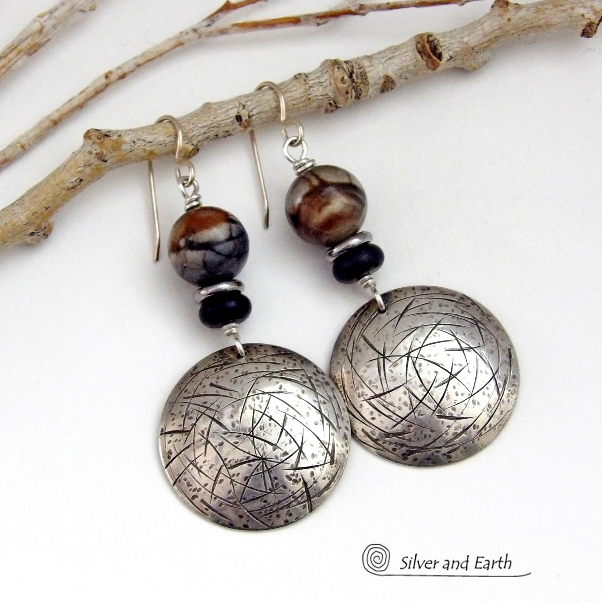 These one-of-a-kind earrings feature handcrafted sterling silver with a hammered and hand stamped texture accented with earthy natural Picasso marble gemstones, black glass and stainless steel beads. This semiprecious stone is found only in southwest Utah. It's named after the famous artist because the natural matrix of geometric lines resembles an abstract painting. The stones in this pair have a beautiful matrix pattern of distinctive swirly lines in black, grey and chocolate brown.