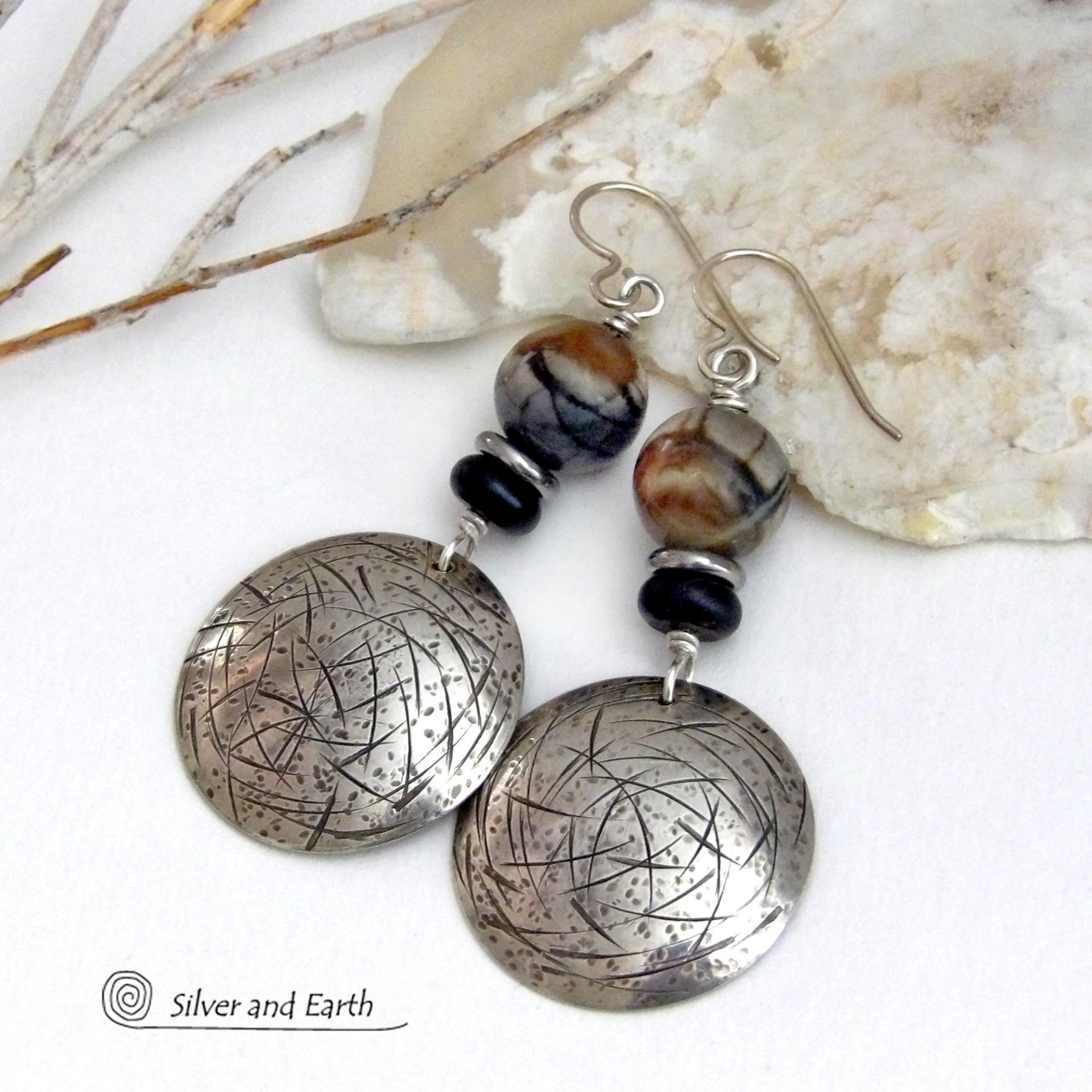 These one-of-a-kind earrings feature handcrafted sterling silver with a hammered and hand stamped texture accented with earthy natural Picasso marble gemstones, black glass and stainless steel beads. This semiprecious stone is found only in southwest Utah. It's named after the famous artist because the natural matrix of geometric lines resembles an abstract painting. The stones in this pair have a beautiful matrix pattern of distinctive swirly lines in black, grey and chocolate brown.