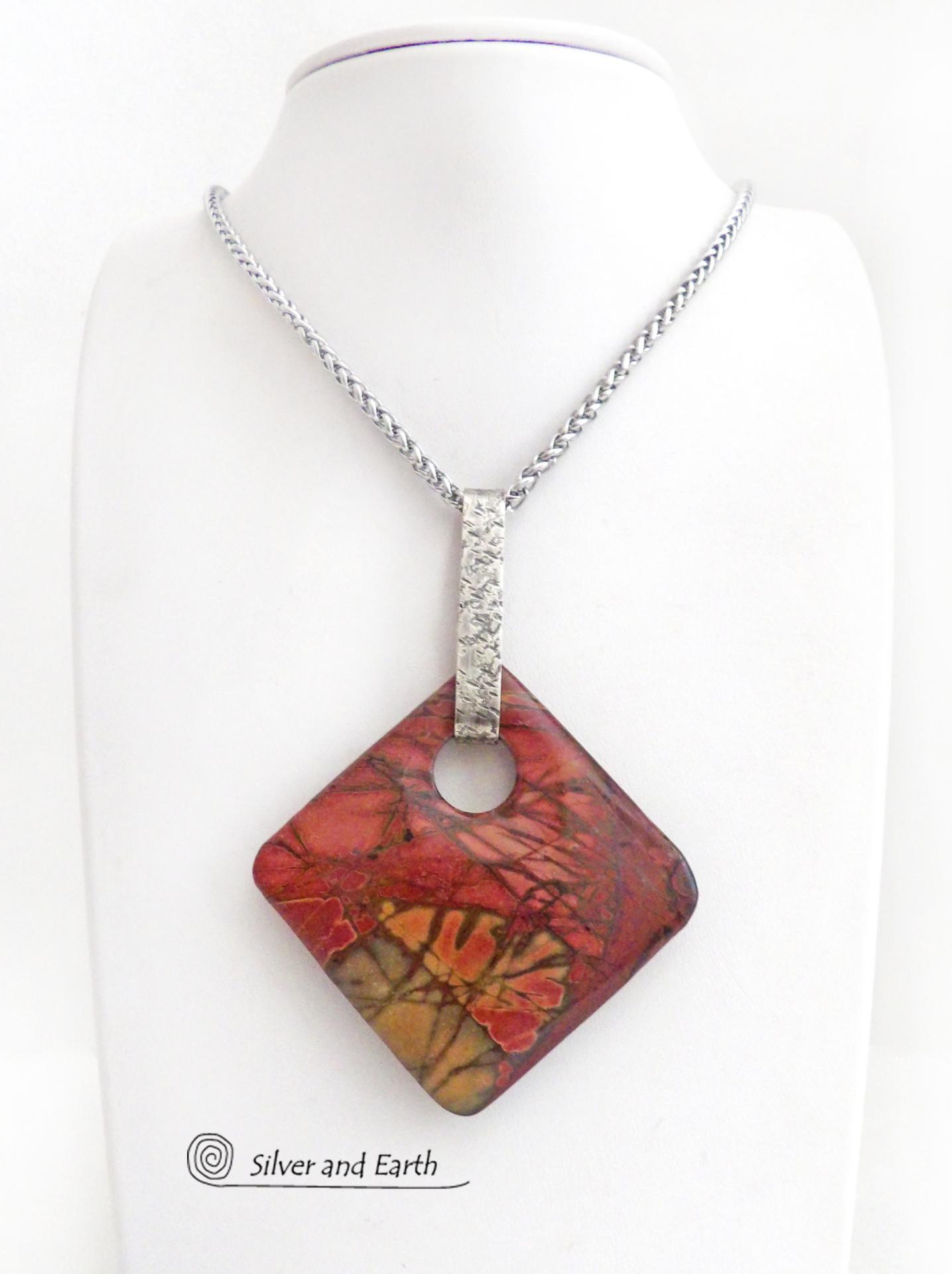 This artisan handcrafted one-of-a-kind necklace features a natural red creek jasper stone accented with a hand forged sterling silver bail with a lightly hammered texture. The stone has a beautiful natural pattern in earthy hues of mossy greens, brick red, brown and orange. It's reversible and can be worn on either side. (See all photos for alternate sides). It makes a great gift for anyone that loves earthy colors and natural stones. The design is unisex so it could be worn by a man or woman.