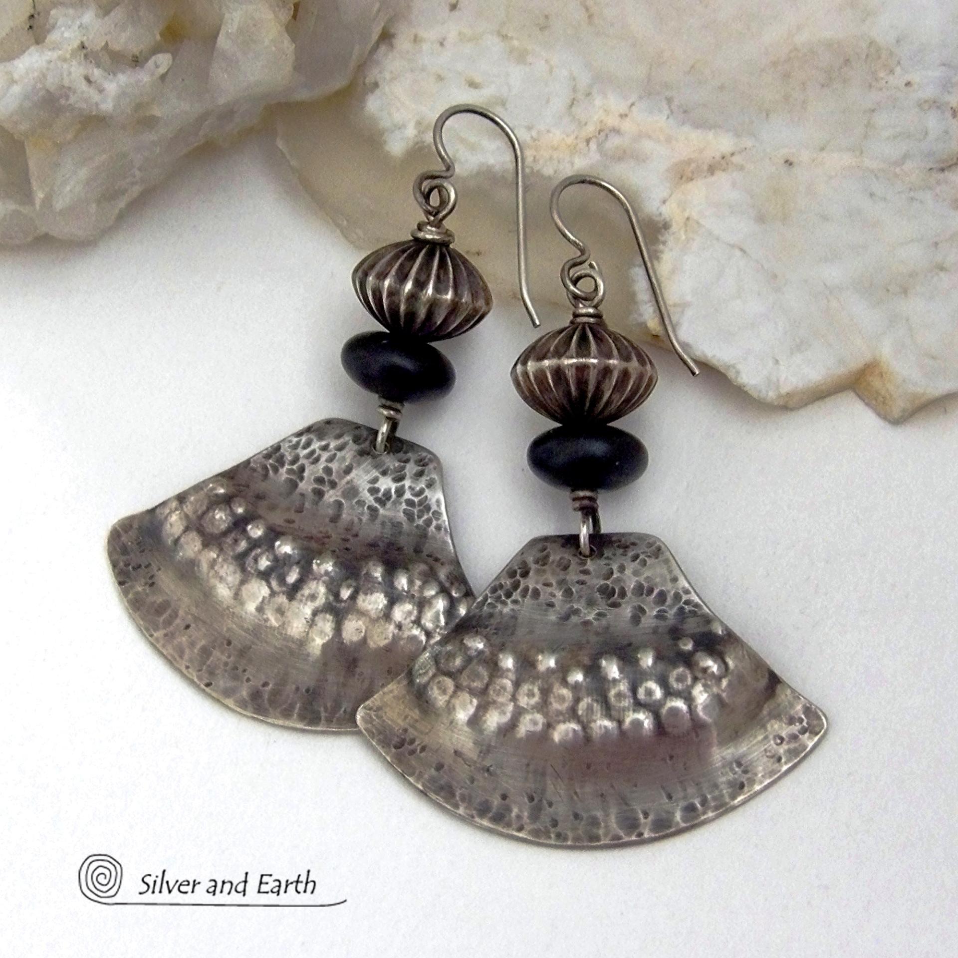 These handcrafted sterling silver earrings have a modern southwestern flair. The sterling shapes have a hammered and stamped texture with an oxidized finish. They are accented with Native Navajo pearl style oxidized sterling silver beads with a rich, corrugated texture and matte black glass beads. Unique and striking, they'll make a bold statement. Handmade in the USA by Silver and Earth Jewelry.