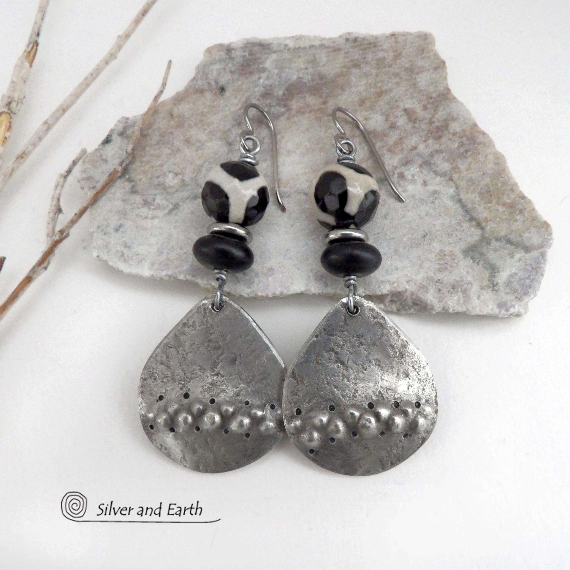 These handcrafted silver pewter earrings have a rustic, hammered texture and are accented with black and off-white Tibetan agate faceted gemstones, black glass and stainless steel beads. Bold and striking, they'll make a unique ethnic tribal statement. Perfect for women that love to wear unique, eye-catching jewelry. Handmade in the USA by Silver and Earth Jewelry.  MEASUREMENTS: Total length of approximately 2-1/2" from top of silver niobium (hypoallergenic) ear wires and 1” at widest point.