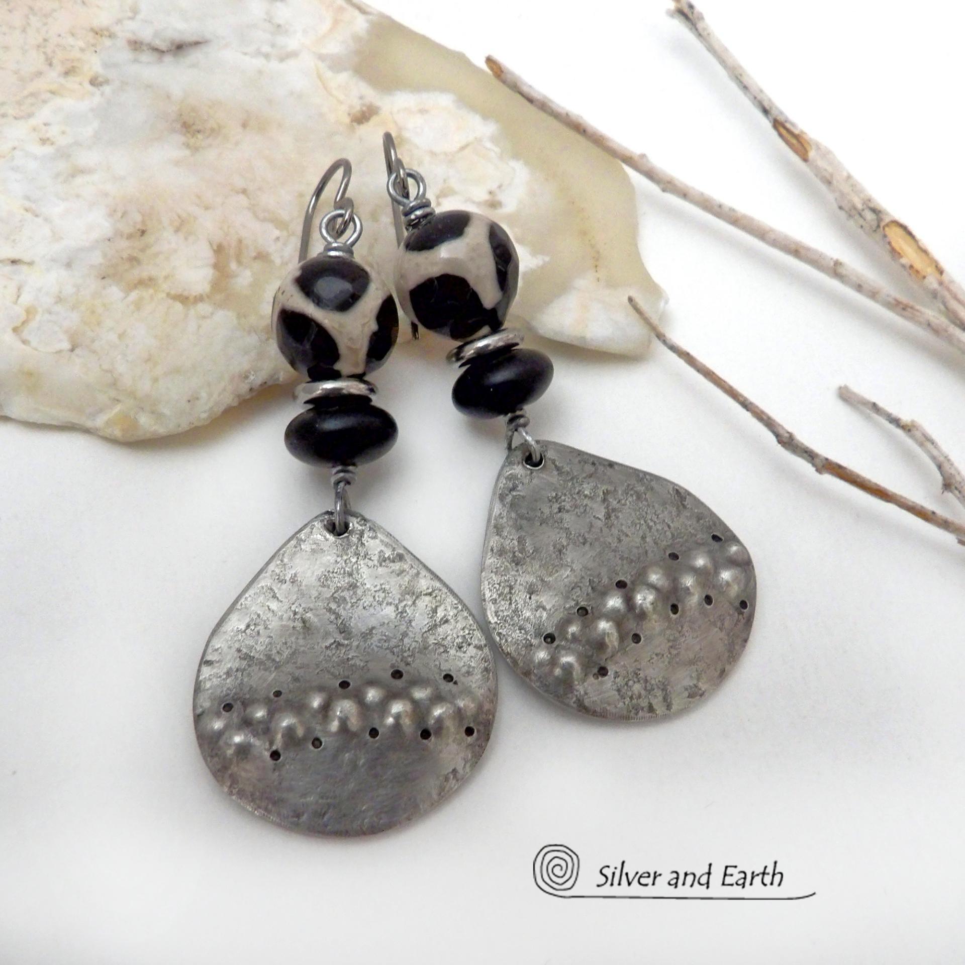 These handcrafted silver pewter earrings have a rustic, hammered texture and are accented with black and off-white Tibetan agate faceted gemstones, black glass and stainless steel beads. Bold and striking, they'll make a unique ethnic tribal statement. Perfect for women that love to wear unique, eye-catching jewelry. Handmade in the USA by Silver and Earth Jewelry.  MEASUREMENTS: Total length of approximately 2-1/2" from top of silver niobium (hypoallergenic) ear wires and 1” at widest point.